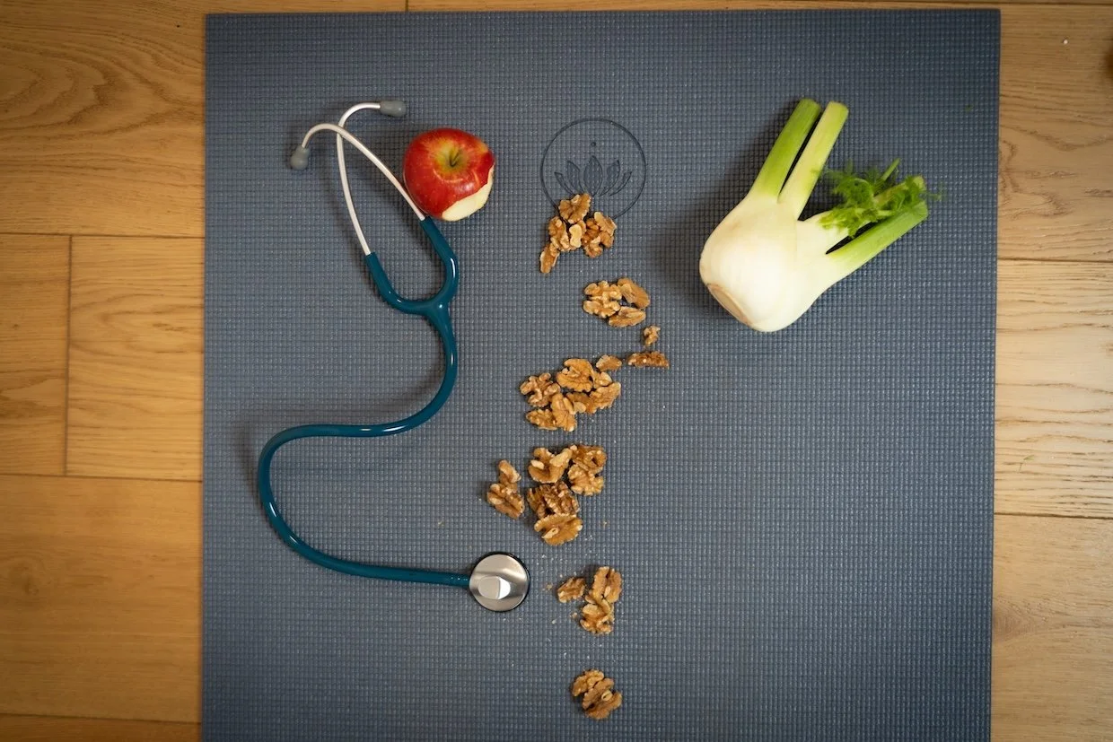 Ein blauer Yogamatte mit einem Apfel, einem Stethoskop, Walnüssen, einem Symbol für Herzgesundheit und einem Knollensellerie auf einem Holztisch.