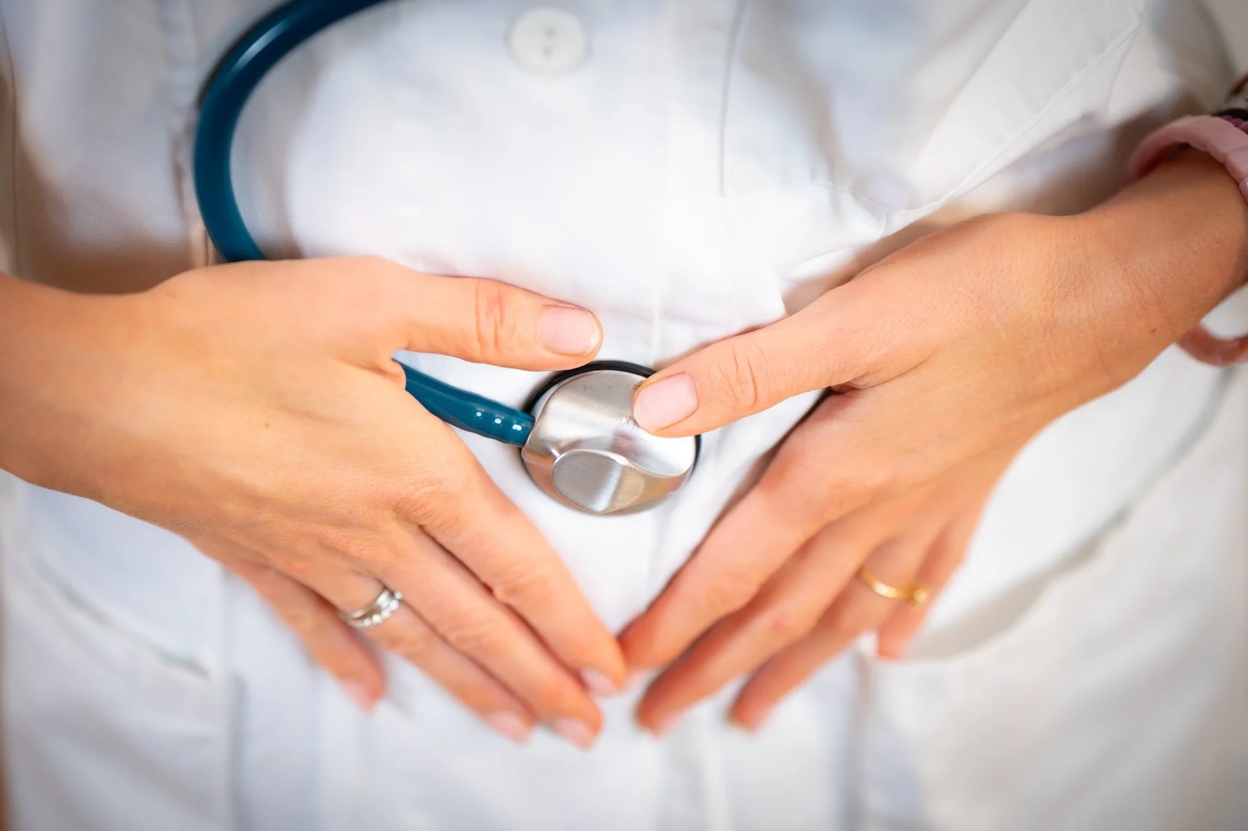 Hände einer medizinischen Fachkraft mit Stethoskop, die die Stelle am Bauch eines Patienten abdecken.