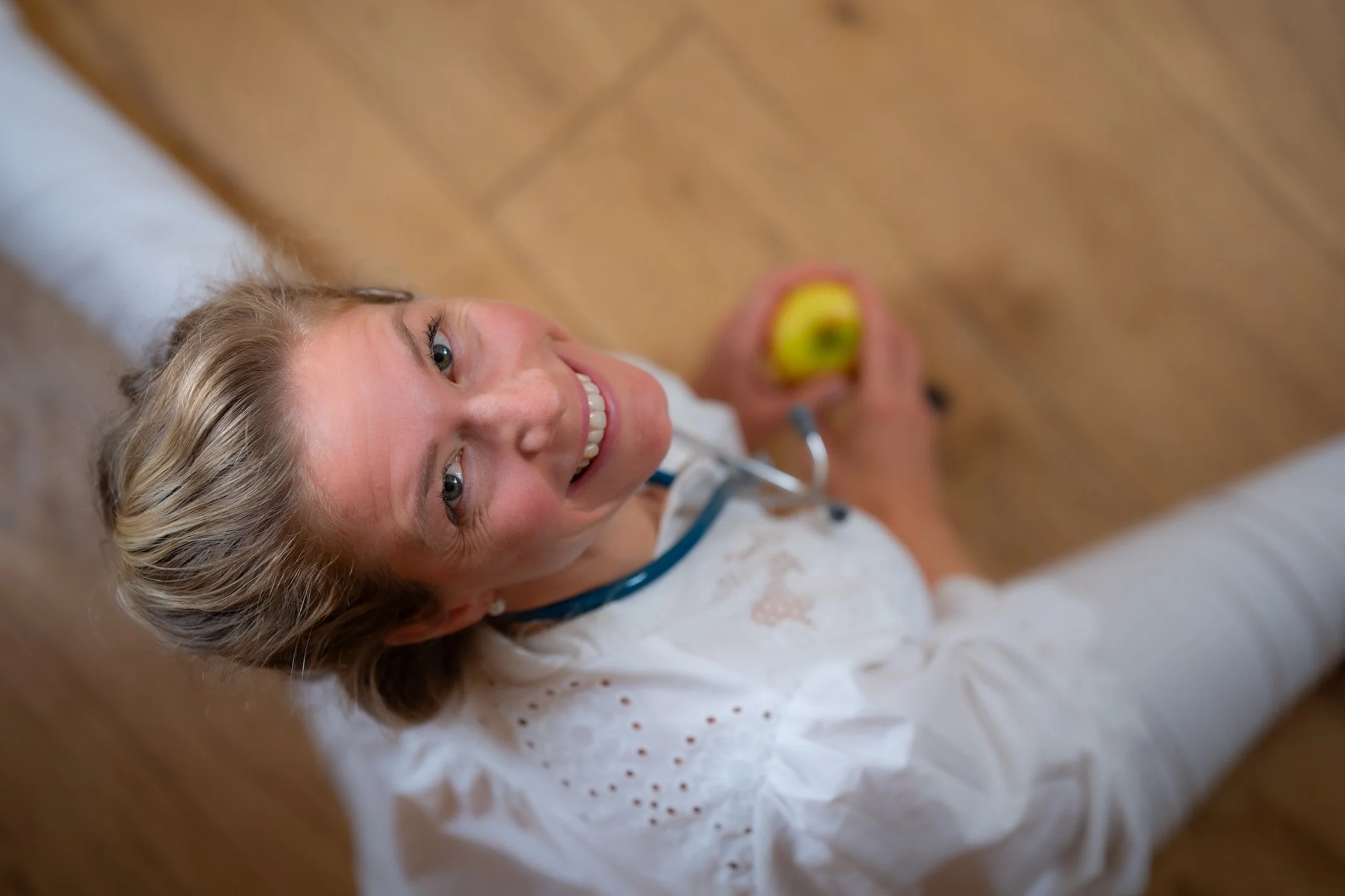 Lächelnde junge Frau mit blondem Haar liegt im Krankenbett, hält einen Ballon und bekommt medizinische Versorgung.