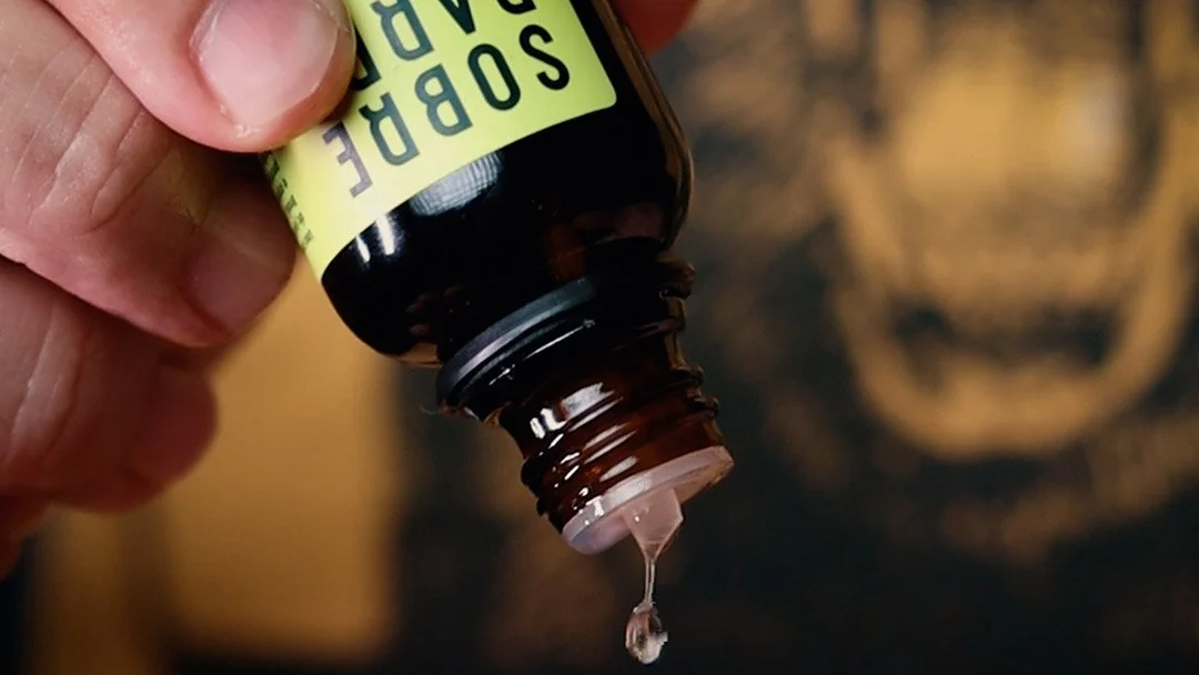 Detalhe de um frasco do óleo de barba Sobrebarba Lemon Drop com uma gota caindo na palma da mão