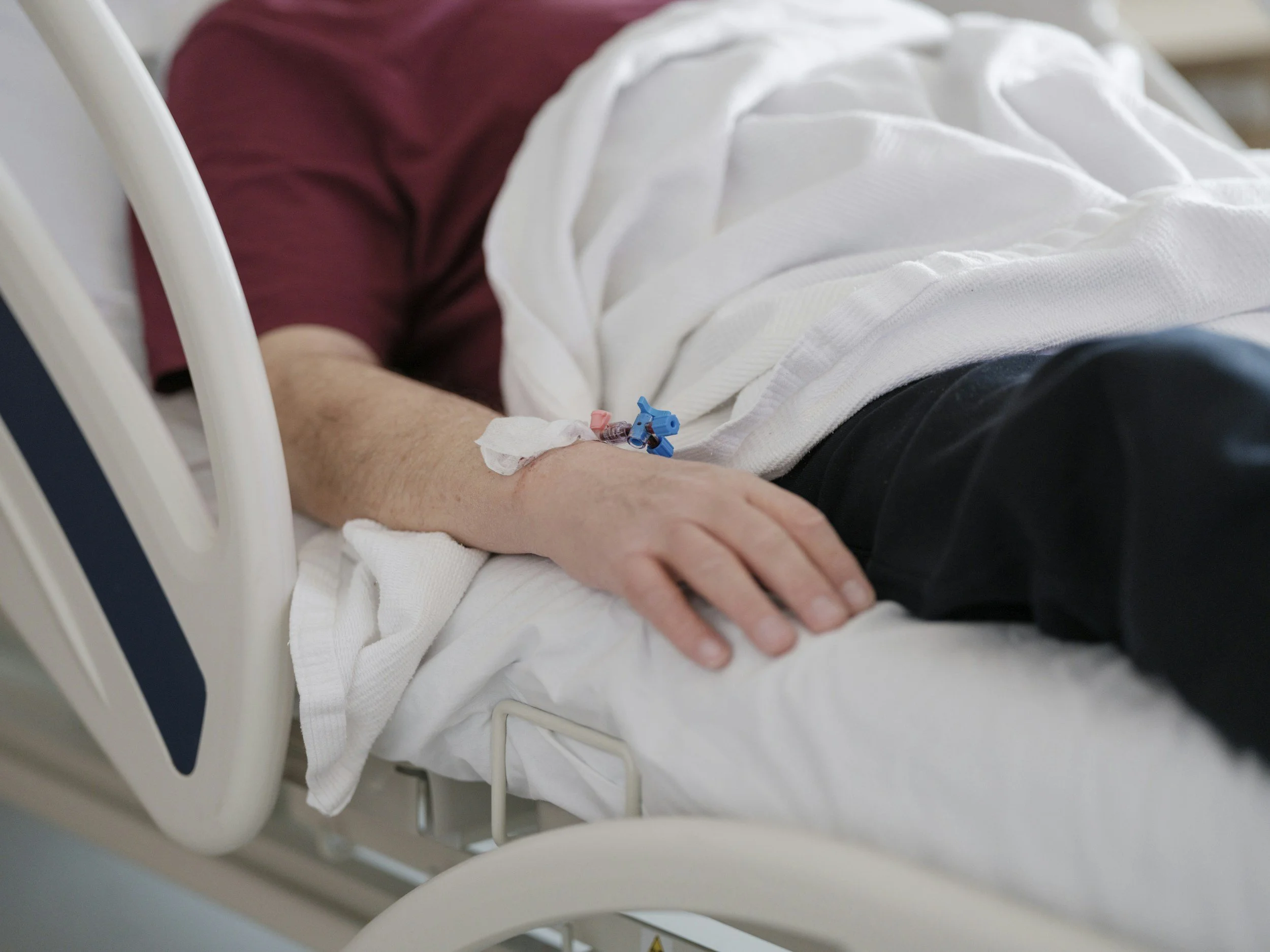 Close-up of a person lying in a hospital bed with an IV inserted in their arm.