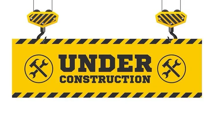 Yellow and black construction sign with the text 'UNDER CONSTRUCTION' and hammer and wrench icons, hanging from two chains.