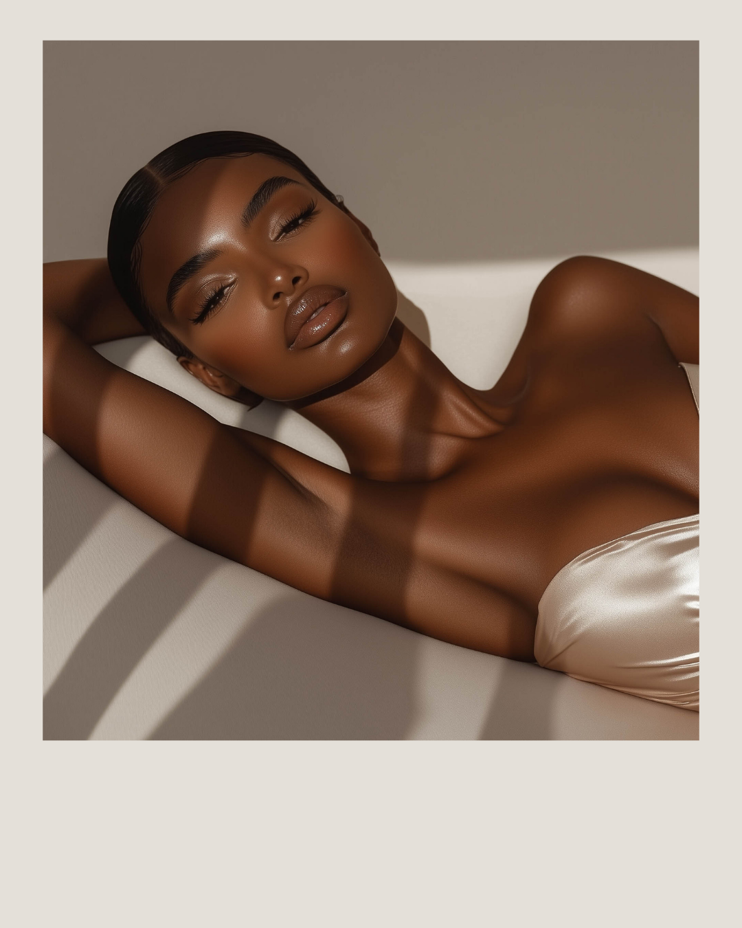 A woman with smooth, dark skin and closed eyes relaxing on a white surface, with shadow lines across her face and body, wearing a satin top.