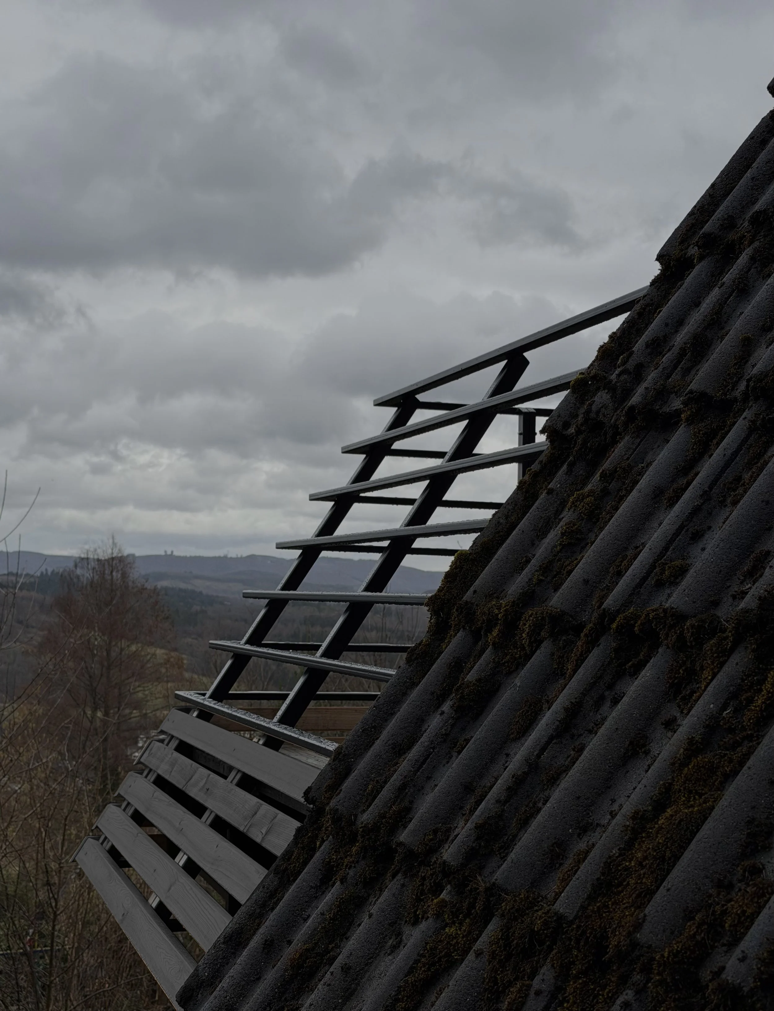 Dach mit Lattung und schneebedeckten Schindeln, blick auf einen bewölkten Himmel und entfernte Berge im Hintergrund.