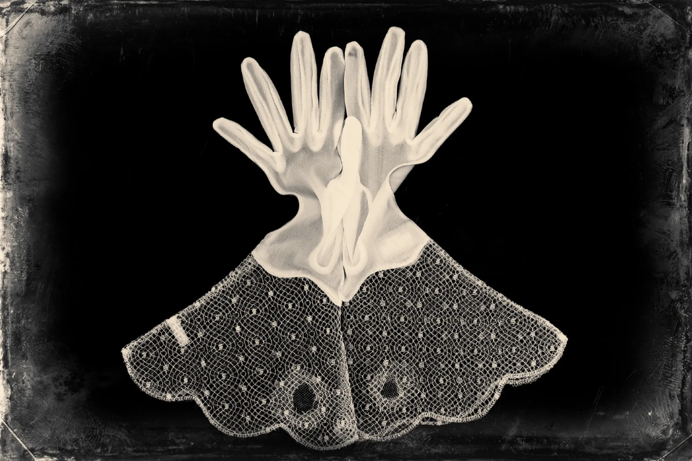 Black and white artistic image of a lace dress with layered gloves placed on top of it, arranged to resemble a butterfly.