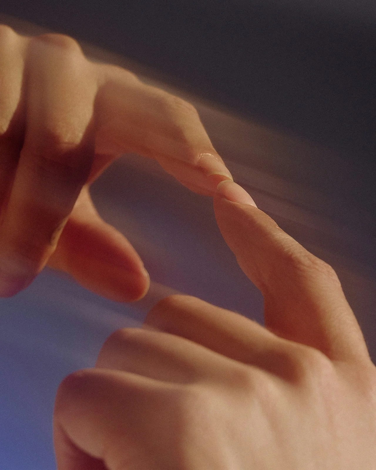 Close-up of human hands reaching towards each other against a blue background.