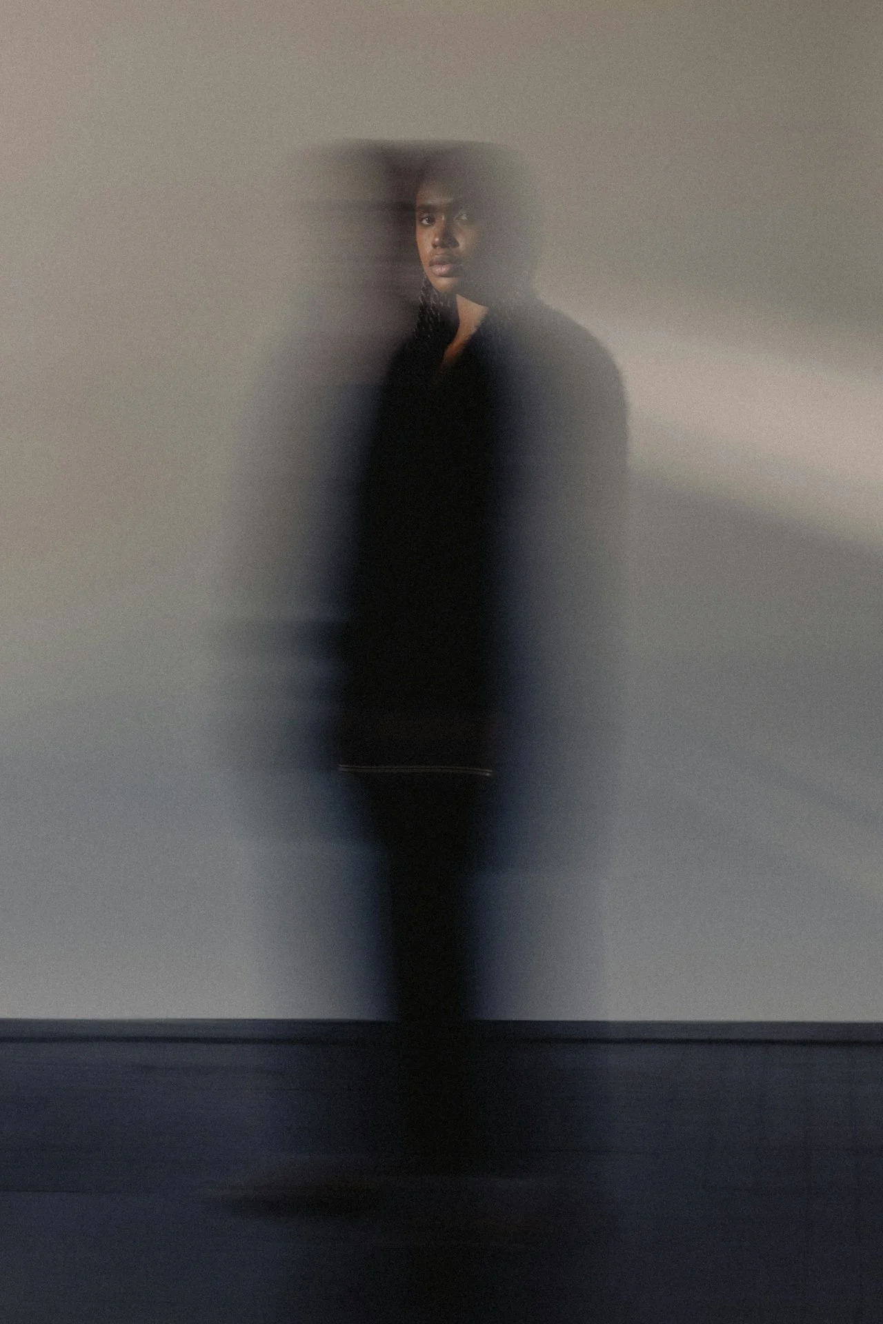 A person standing against a wall, partially obscured by a semi-transparent surface, creating a blurred effect.