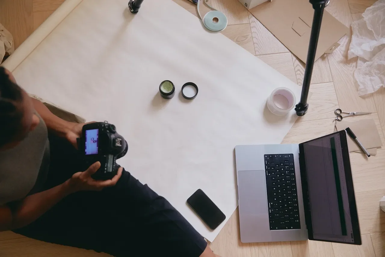 Bird's eye view of a creative workspace showing a hand holding a DSLR camera alongside a laptop and design accessories, representing the active build day process at Knight Theory™ Los Angeles web design studio.