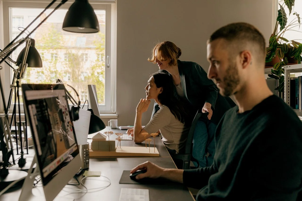 Three creative professionals gathered around a monitor reviewing design work in a bright studio space, representing the collaborative foundational brand design phase of Knight Theory™'s Full Court one-month brand transformation package.