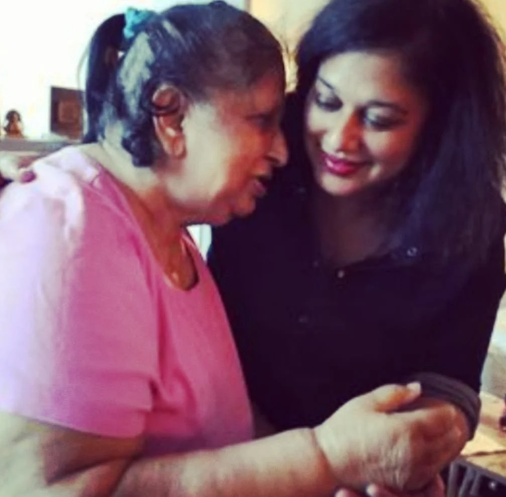 Two women are close together, sharing a moment of affection while looking at each other's hands.