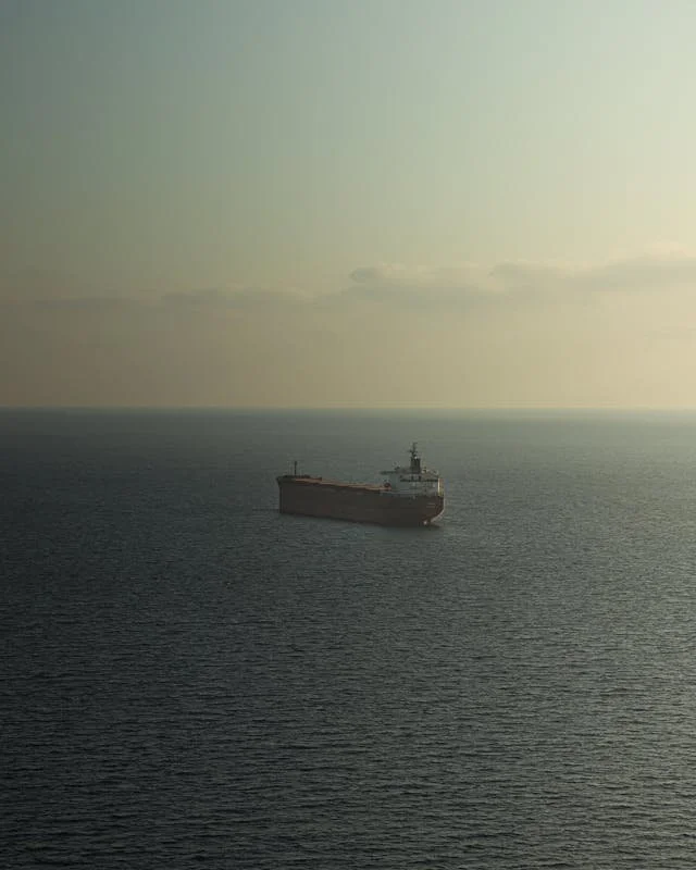 A large cargo ship sailing in the ocean under a partly cloudy sky.