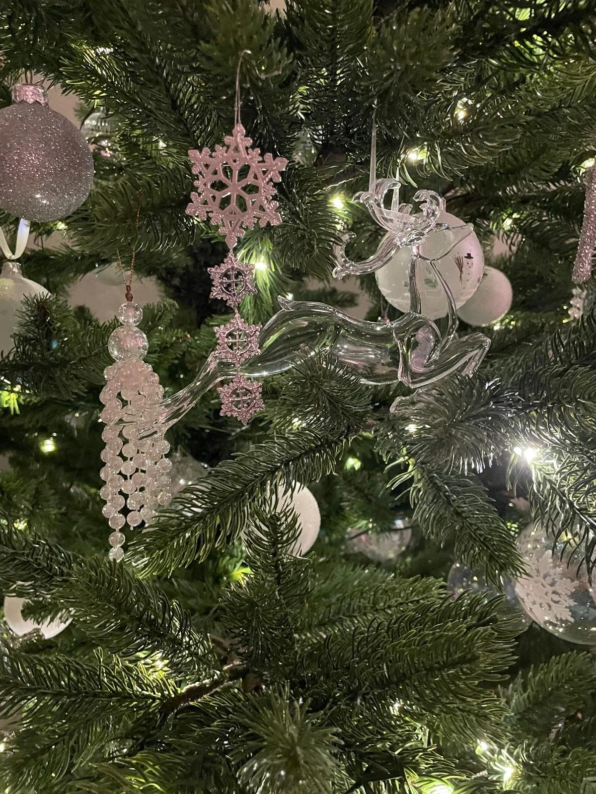 Decorated Christmas tree with glass reindeer ornament, white snowflake ornaments, and white baubles, illuminated by small white lights.