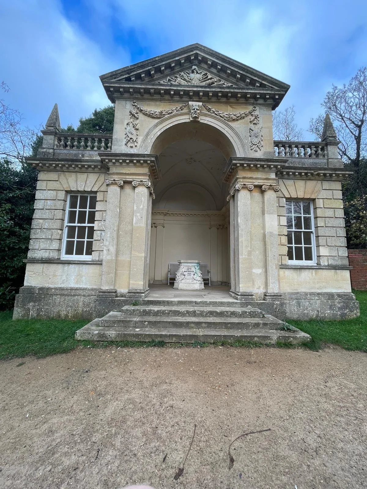 An old stone mausoleum with classical architecture, featuring columns, arches, and decorative sculptures. It has stairs leading up to an open area with a memorial inside.