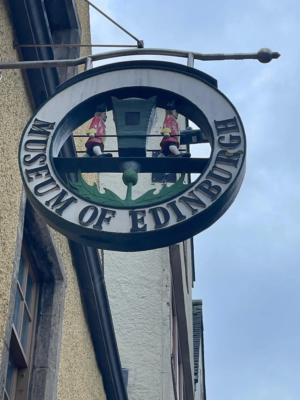 Hanging sign of the Museum of Ediburgh with two small toy soldiers on top inside a circular frame.