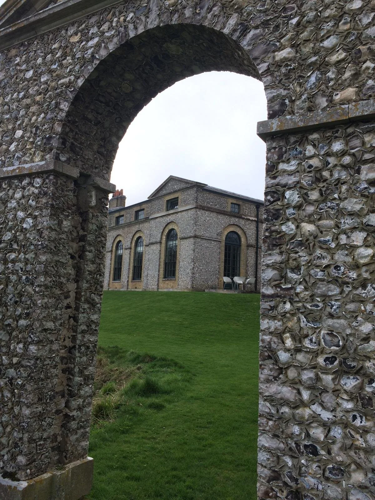 Stone archway overlooking a historic brick building with tall arched windows and a well-maintained grassy lawn.