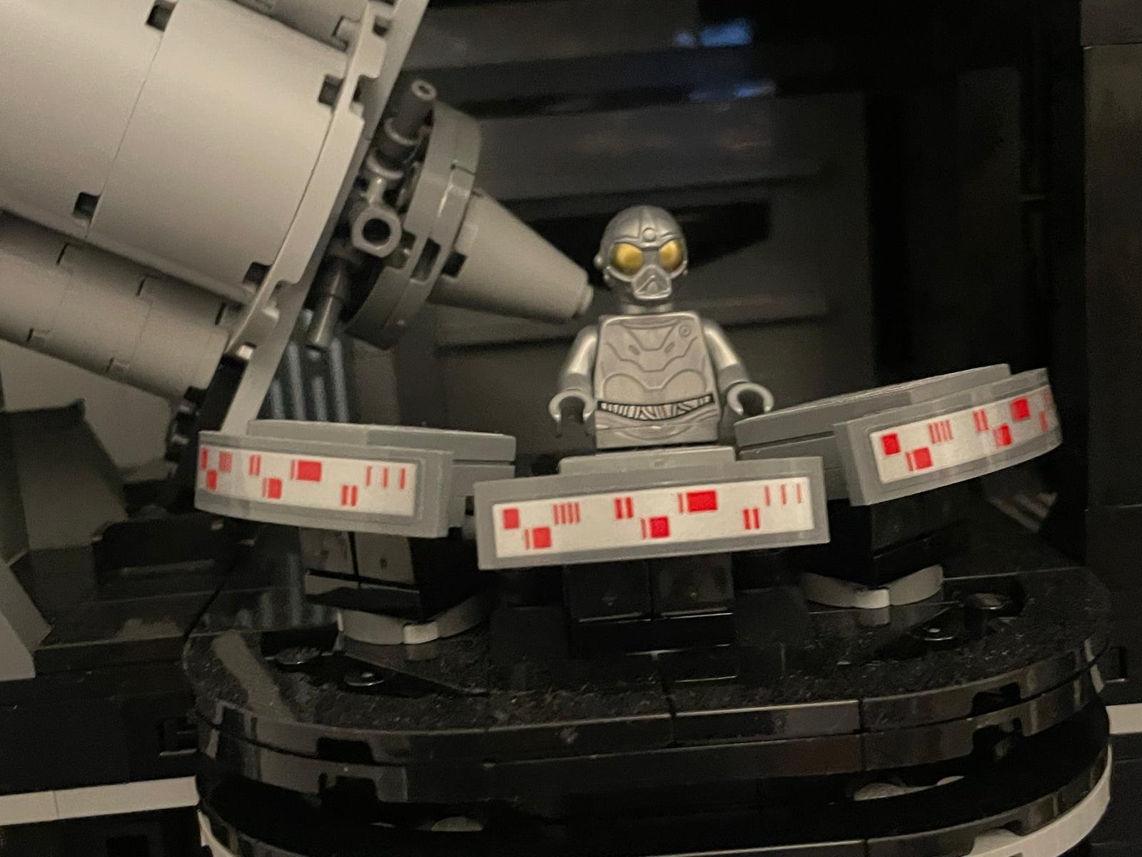 A LEGO minifigure wearing a helmet and armor, standing inside a spaceship or advanced vehicle with mechanical and electronic components.