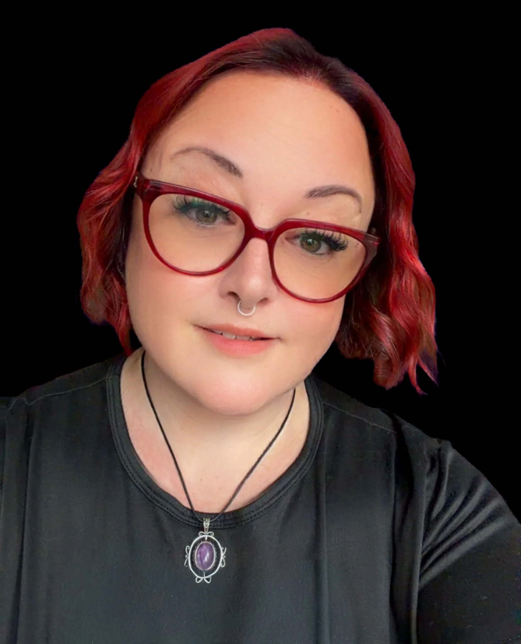 A woman with short red hair and glasses, wearing a black shirt and a necklace with a purple pendant, smiling against a black background.