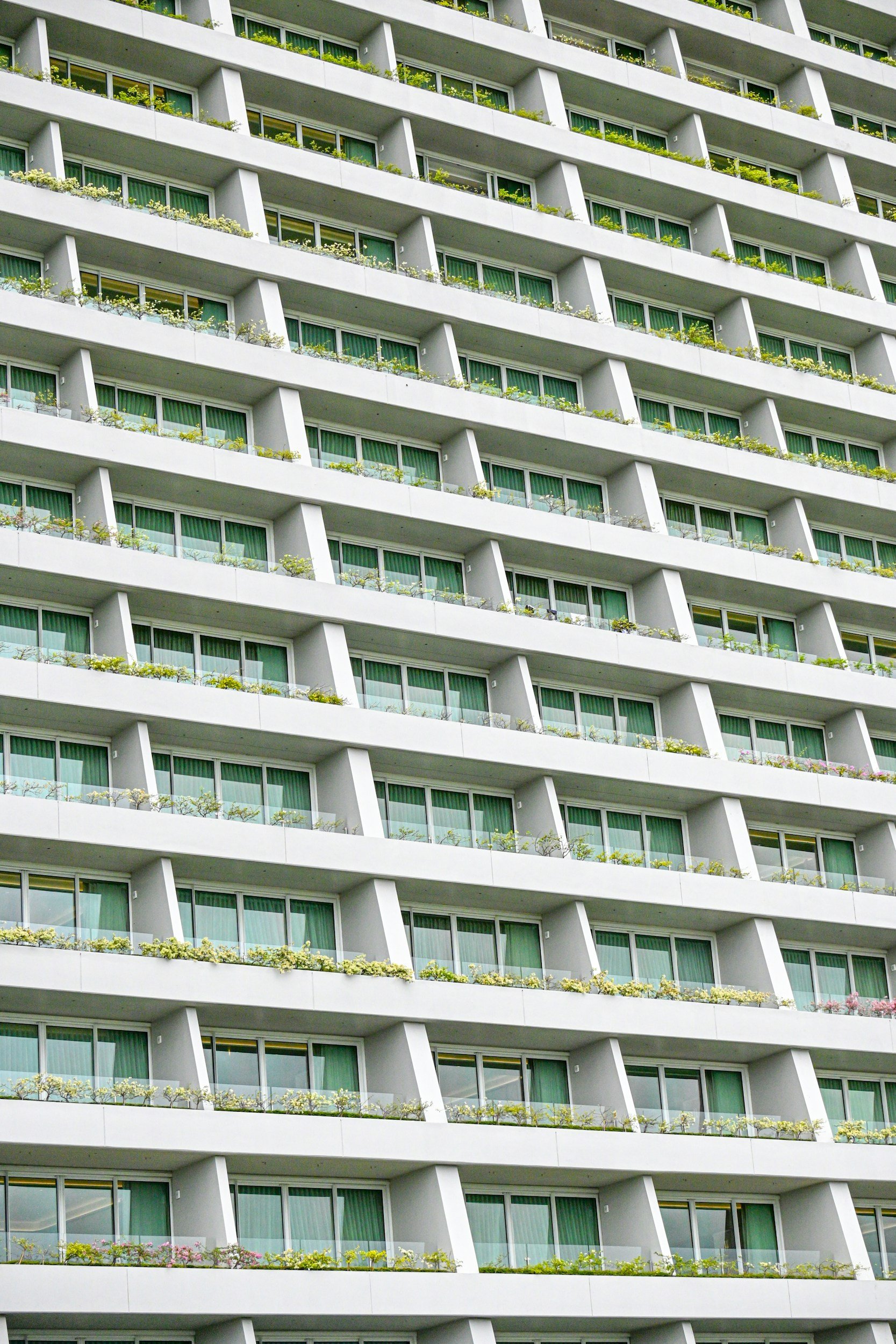 Blick auf mehrere Balkone eines modernen weißen Hochhauses, jedes mit grünen Gartenpflanzen und Blumen.