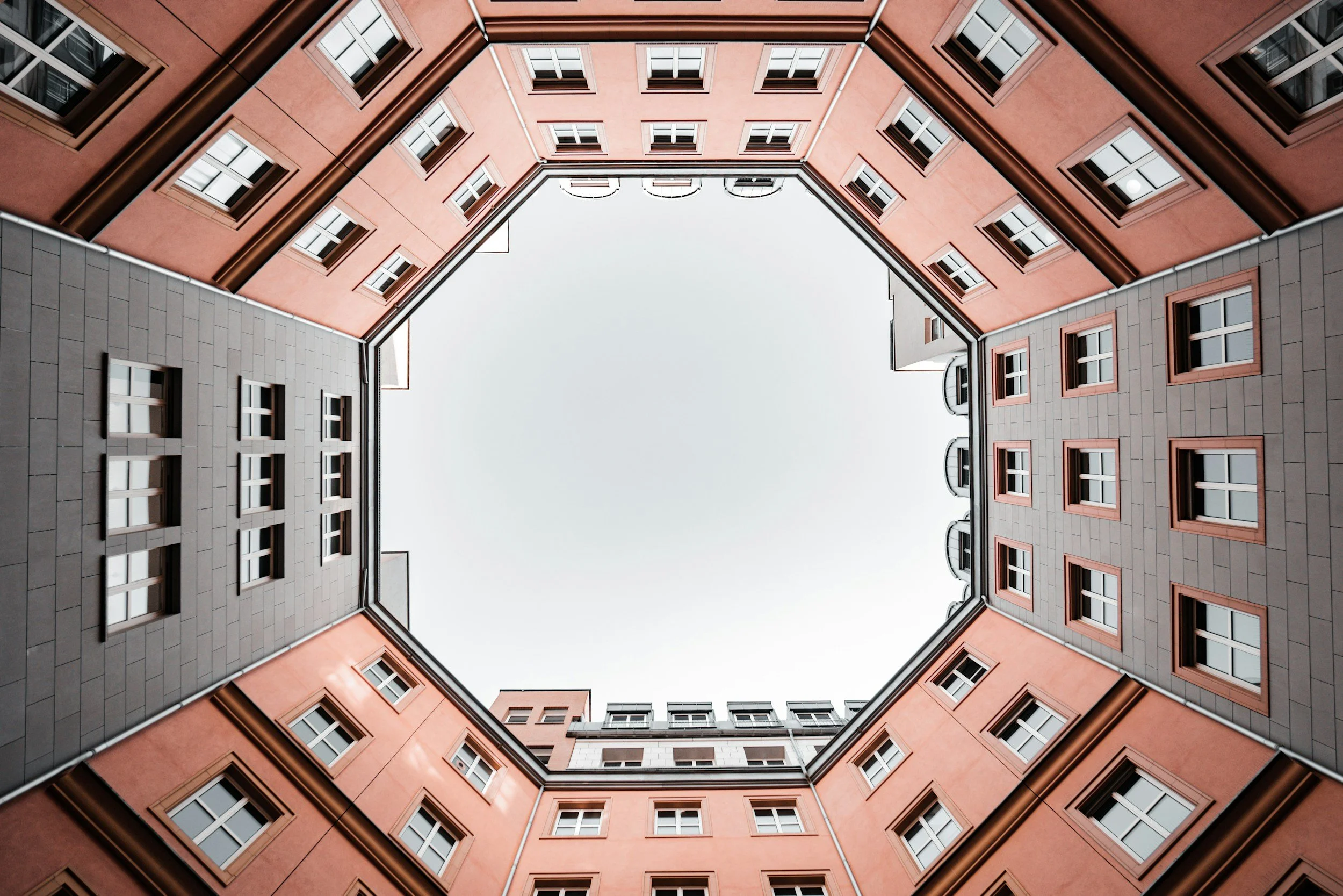 Innenhof eines mehrstöckigen roten Gebäudes mit mehreren Fenstern, Blick nach oben zum Himmel.
