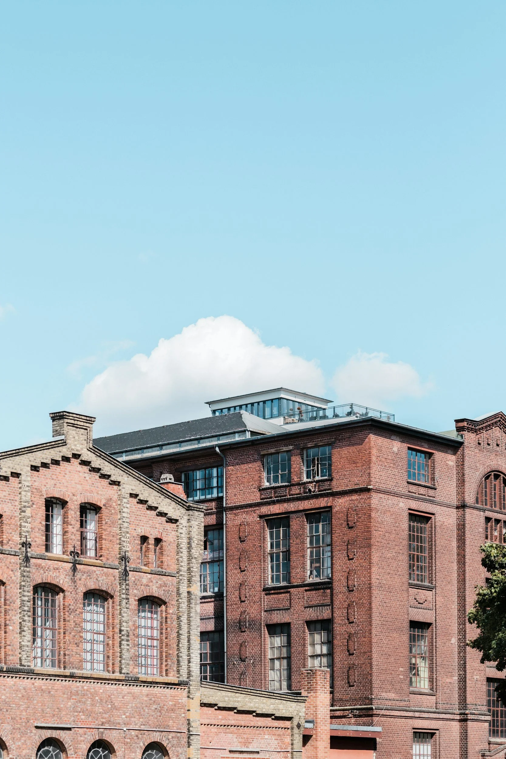 Mehrstöckige historische Backsteingebäude mit großen Fenstern vor einem blauen Himmel mit wenigen Wolken.