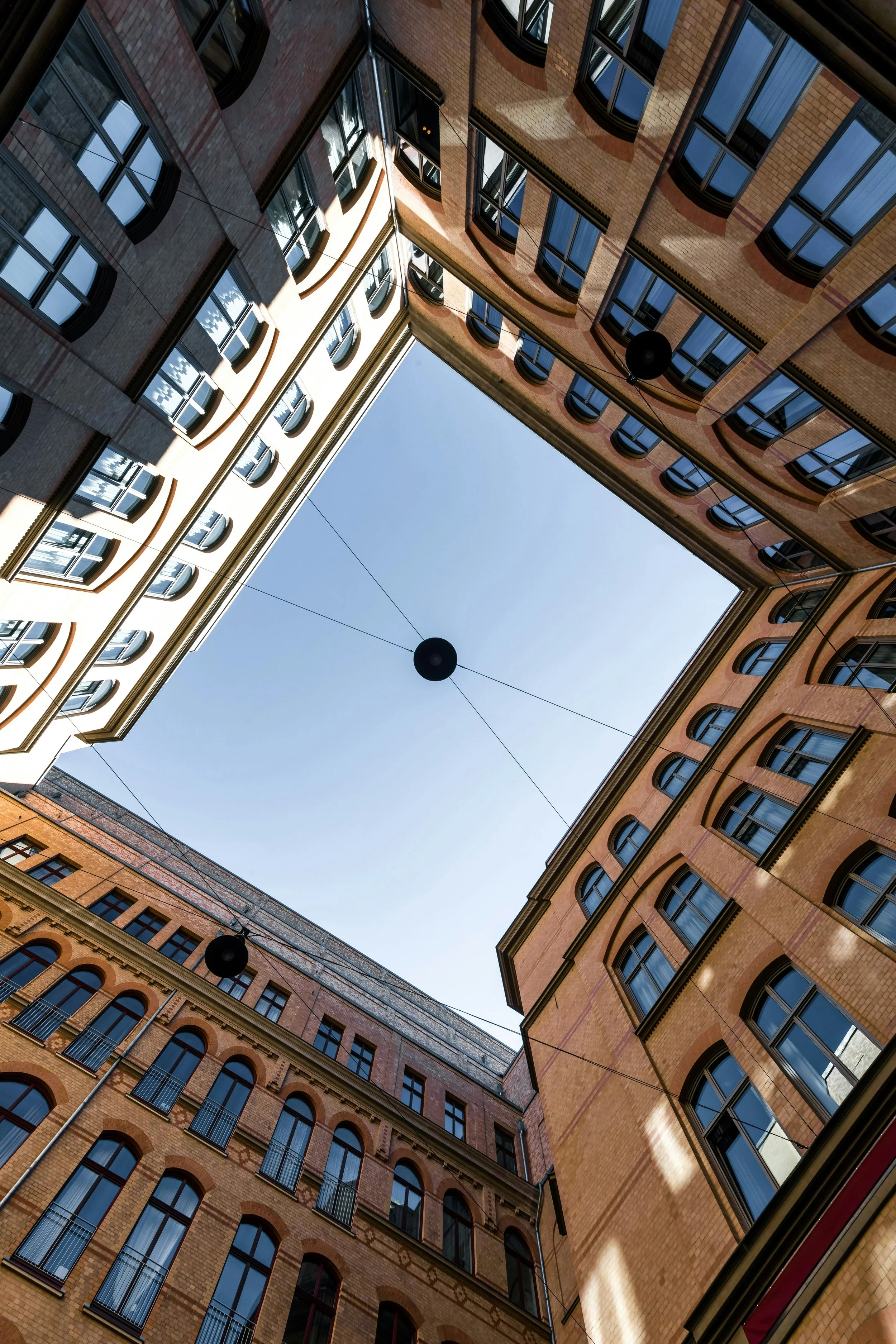 Ansicht eines traditionellen mehrstöckigen, hellbraunen Backsteingebäudes mit vielen Fenstern und Balkonen, aufgenommen von unten mit Blick in den Himmel.