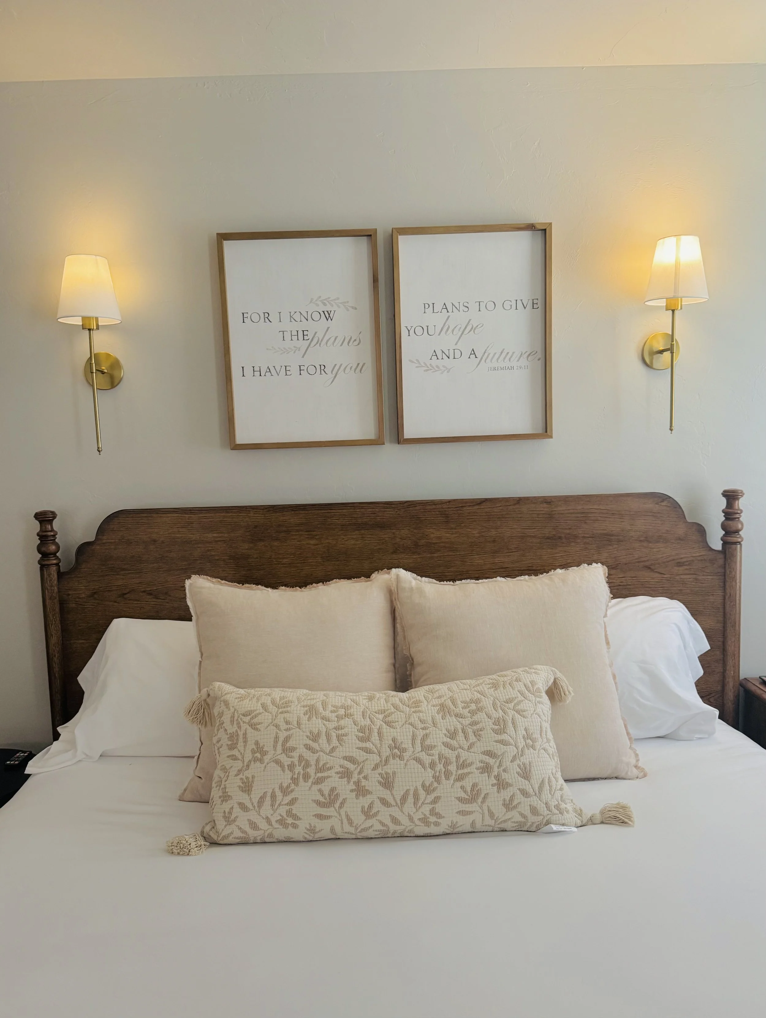 Serene master bedroom with farmhouse wooden headboard, beige pillows, inspirational scripture art, and warm lighting at Grandview Farmhouse Stillwater OK