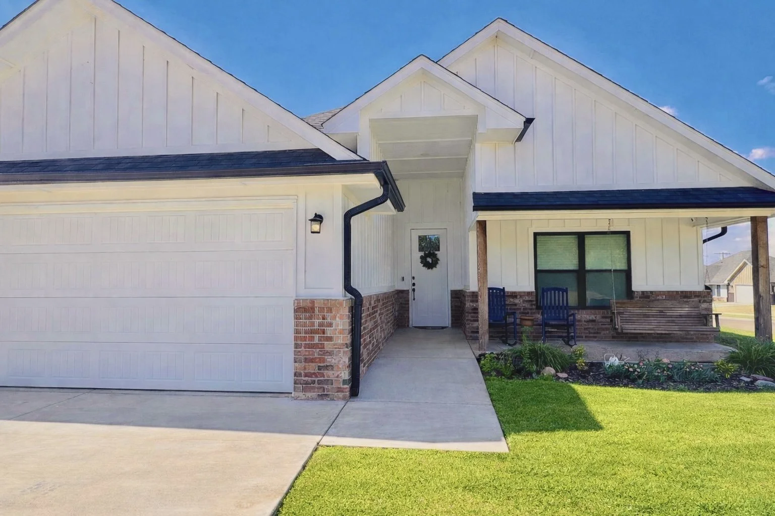 Modern farmhouse exterior of Grandview Farmhouse in Stillwater, Oklahoma featuring white siding, covered front porch with rocking chairs, attached garage, and welcoming entryway