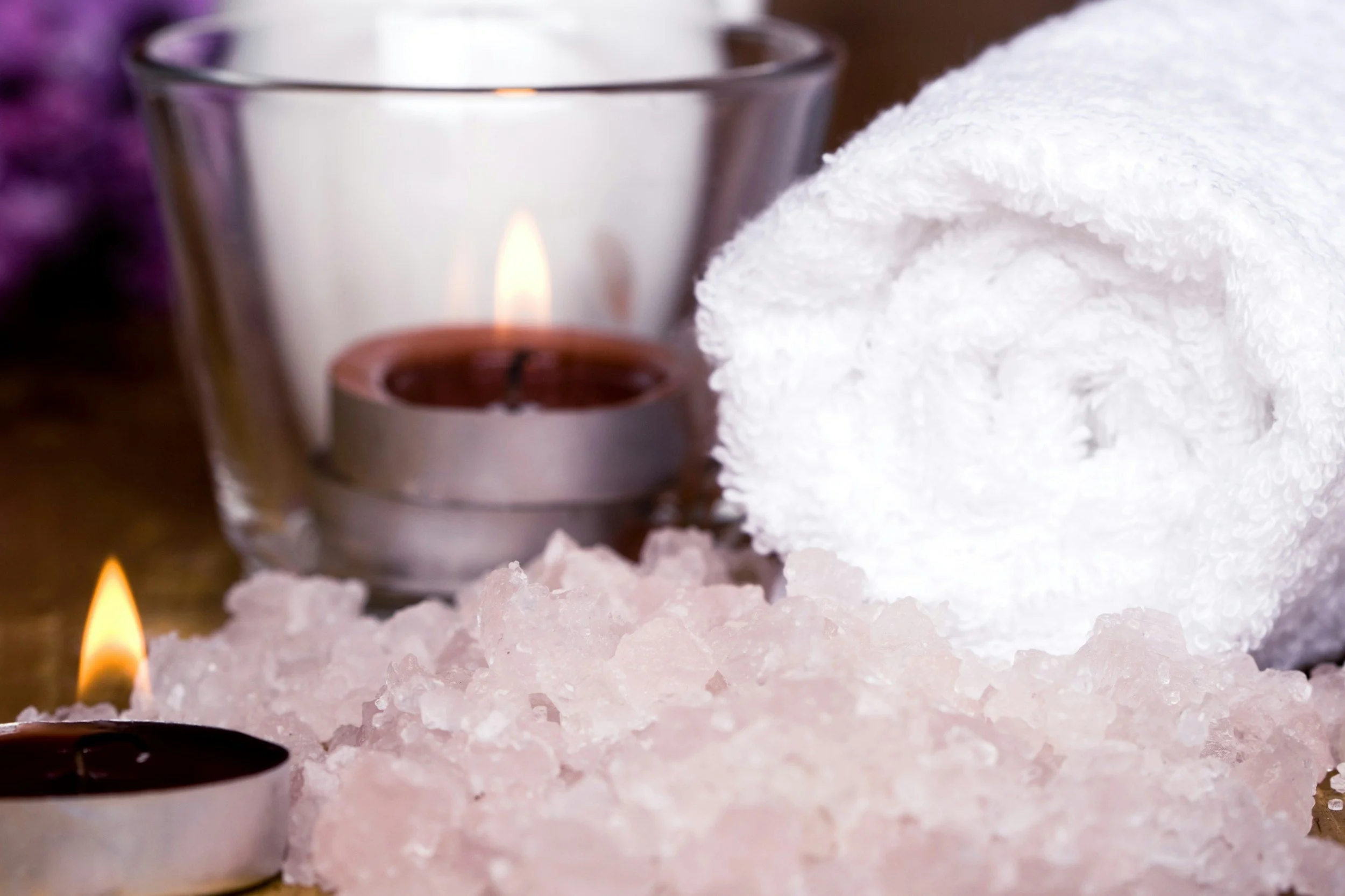 White bath salts with tealight candles and a white towel in the background for a spa setting.
