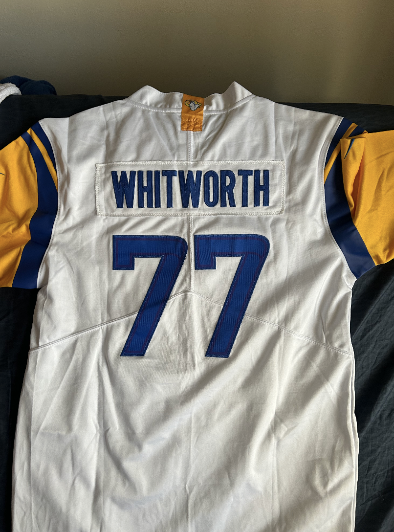 White and yellow sports jersey with 'WHITWORTH' and the number '77' on the back, lying on a dark surface.