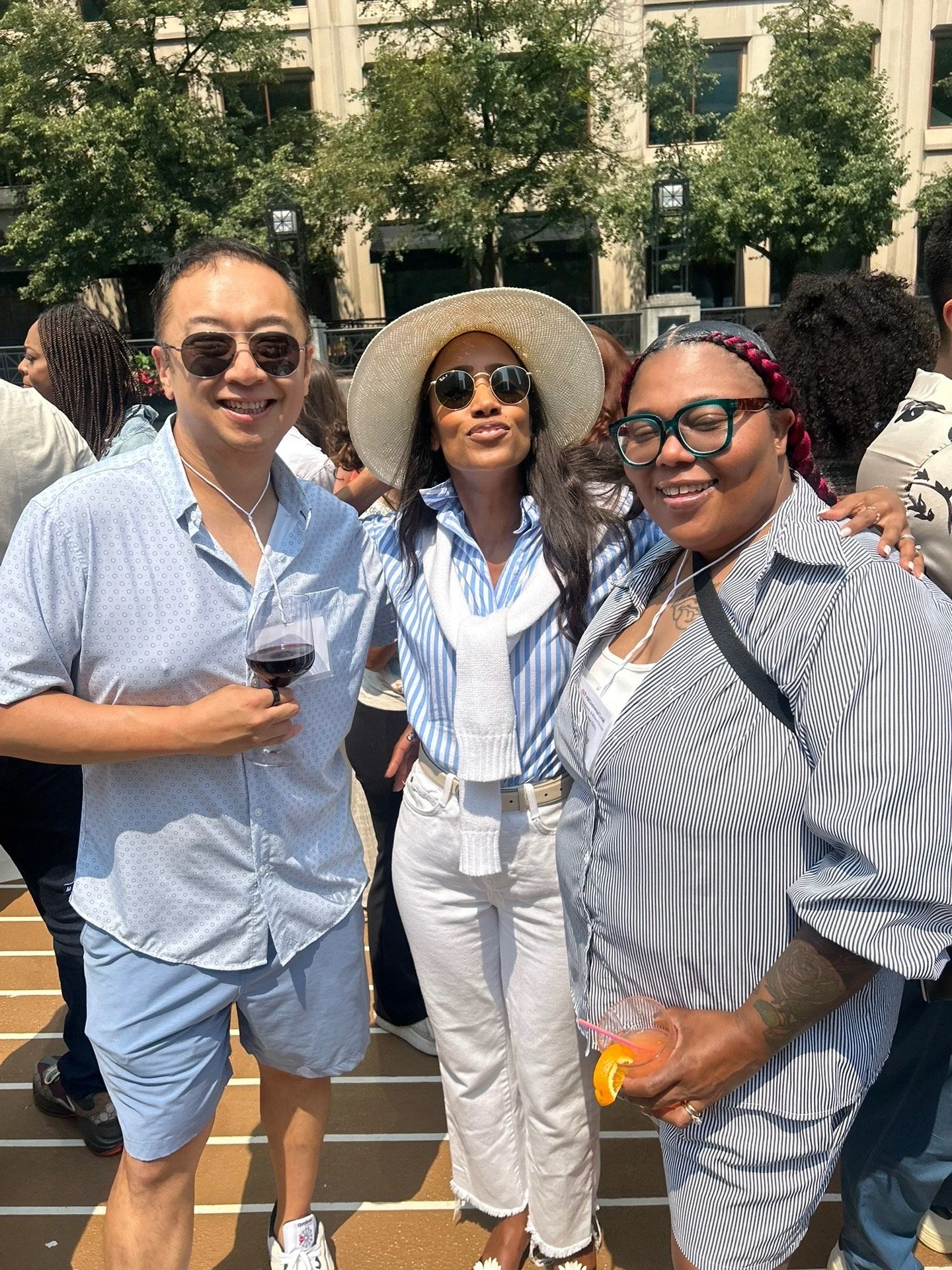 Three women standing together at an outdoor social event, smiling and holding drinks.
