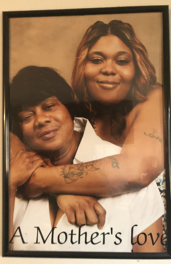 Two women, one older and one younger, hugging and smiling in a framed photograph titled 'A Mother's Love'.