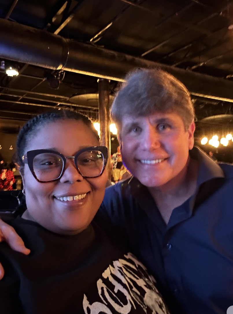 Two smiling people taking a selfie in a dimly lit venue, with dark wooden beams on the ceiling and warm lights in the background.