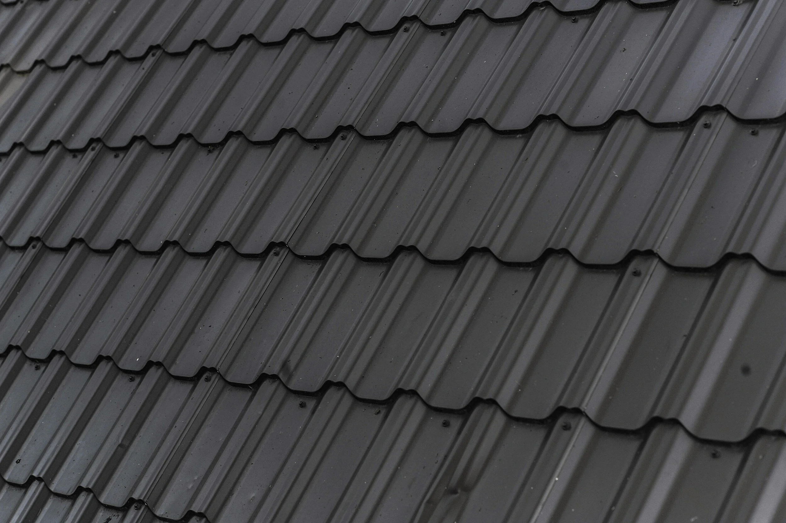 Close-up of black metal roof shingles arranged in overlapping rows.