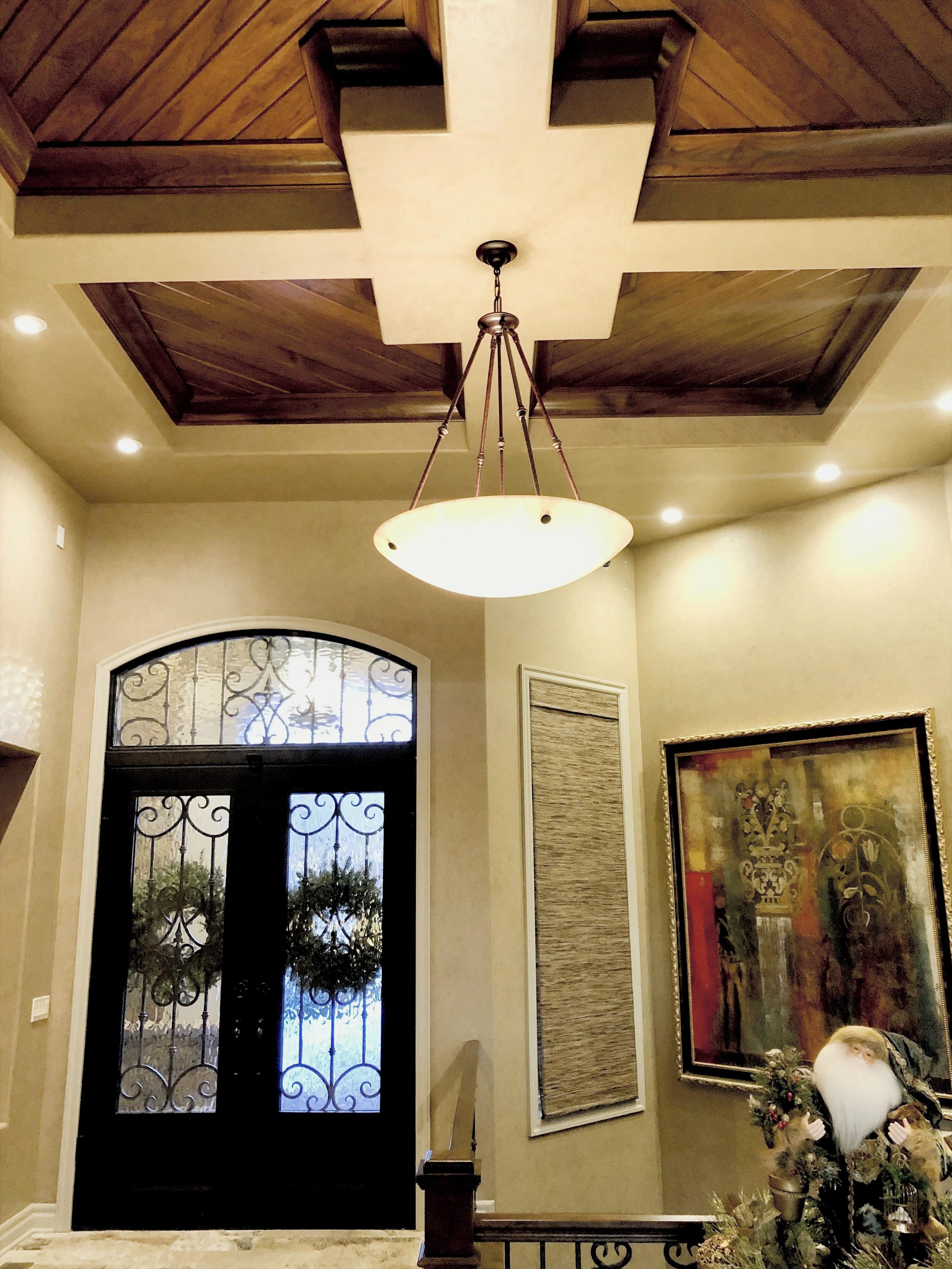 Interior view of a home entryway with a decorative front door, a hanging ceiling light, a framed painting, and a Santa Claus decoration.