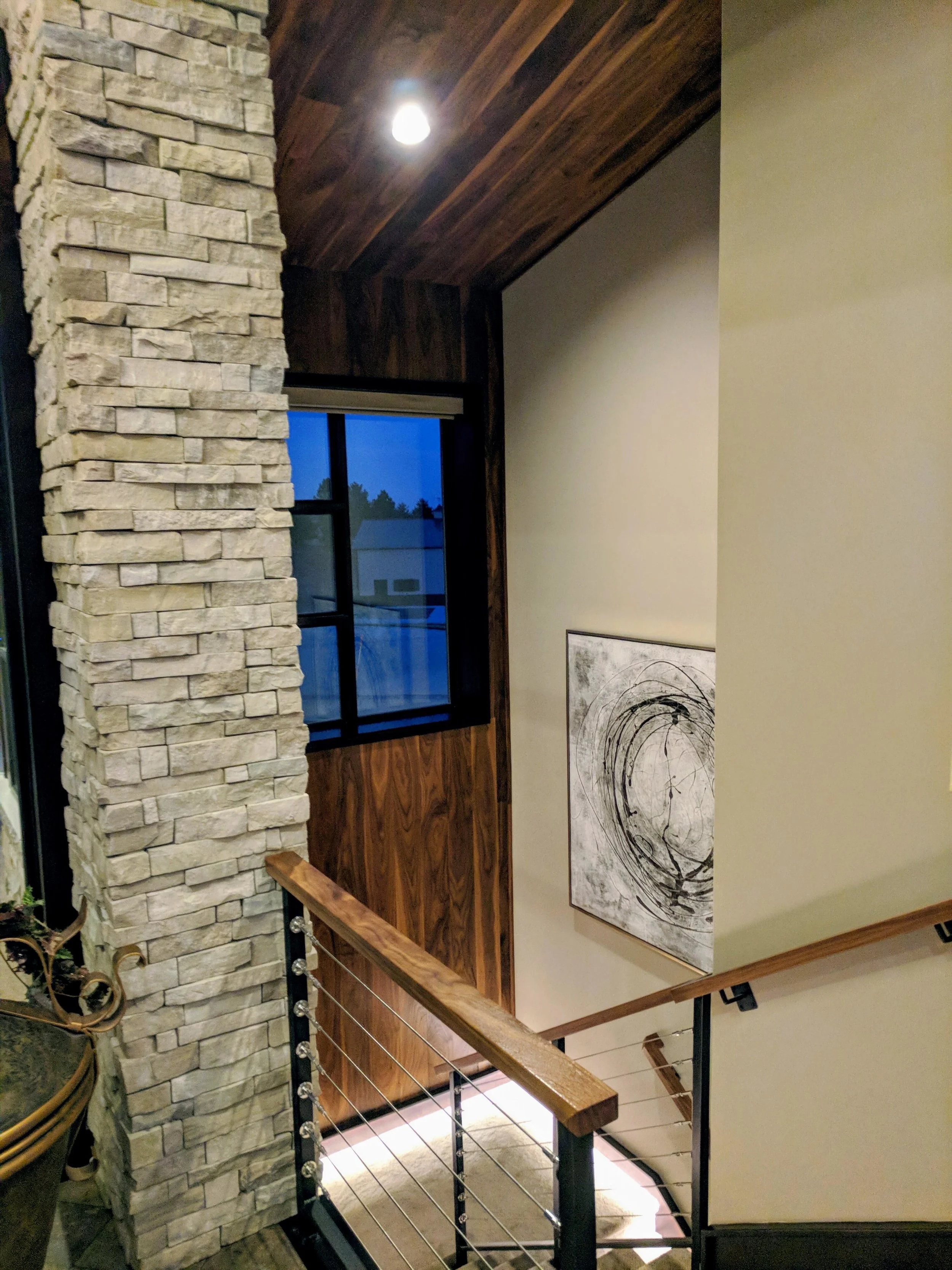 Interior view of a staircase area with a stone wall, wooden ceiling, window, and artwork on the wall.