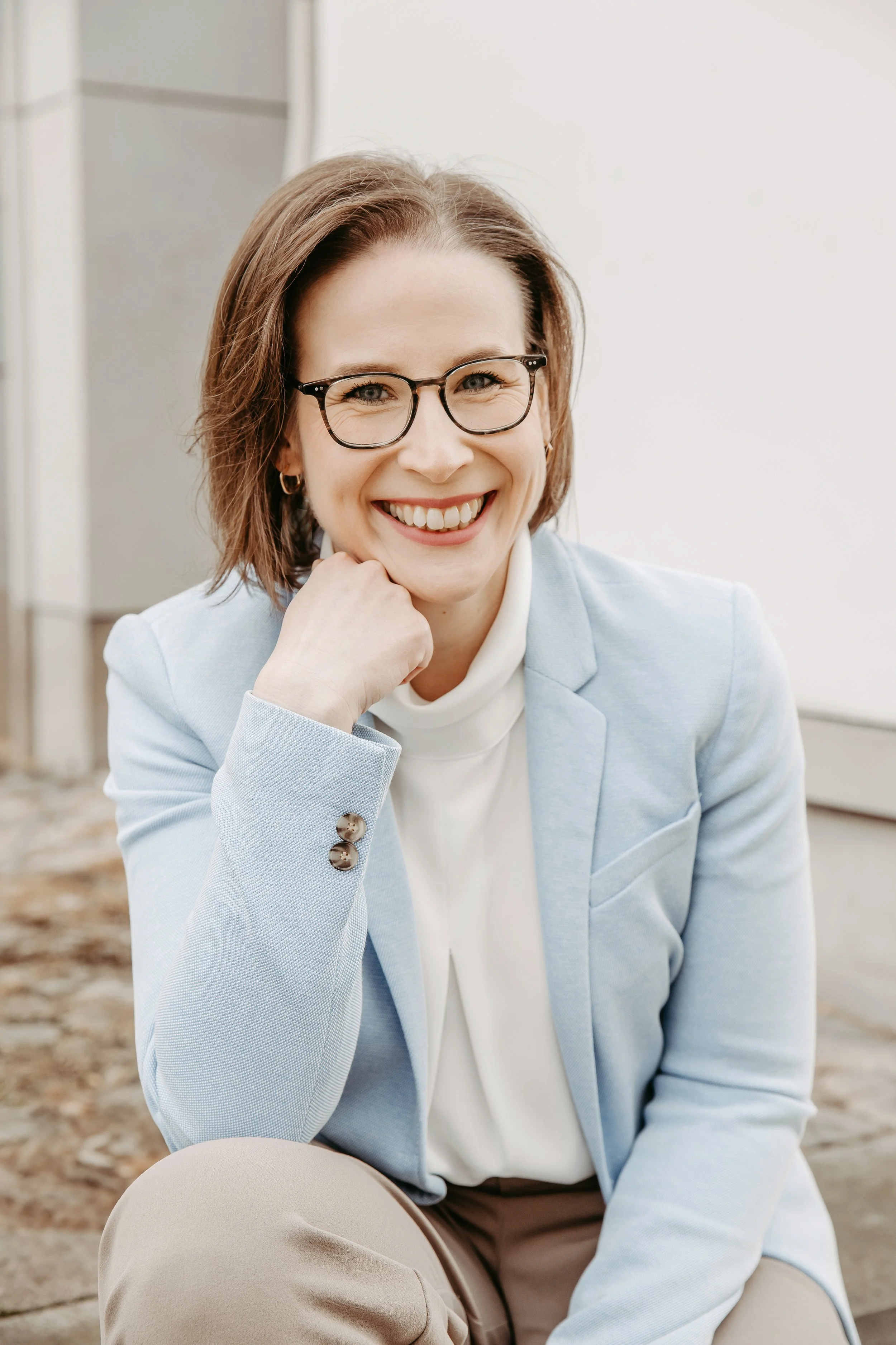 Lächelnde Frau mit Brille in hellblauer Jacke im Freien