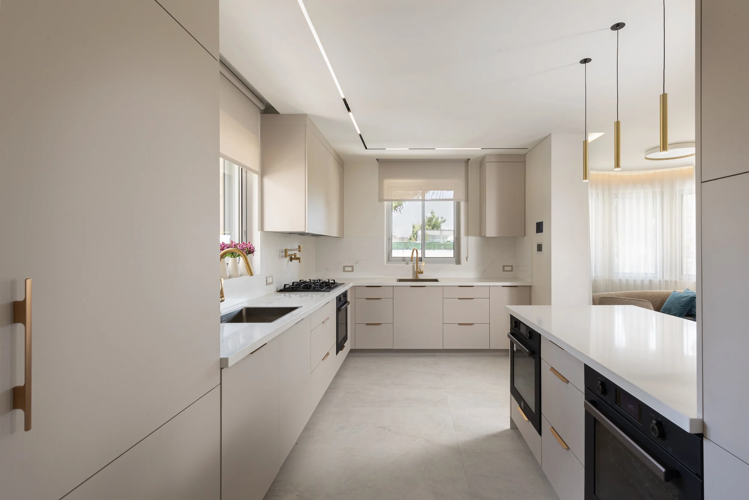 Modern kitchen with white cabinetry, a black oven, gold faucet, and large window with sheer curtains.