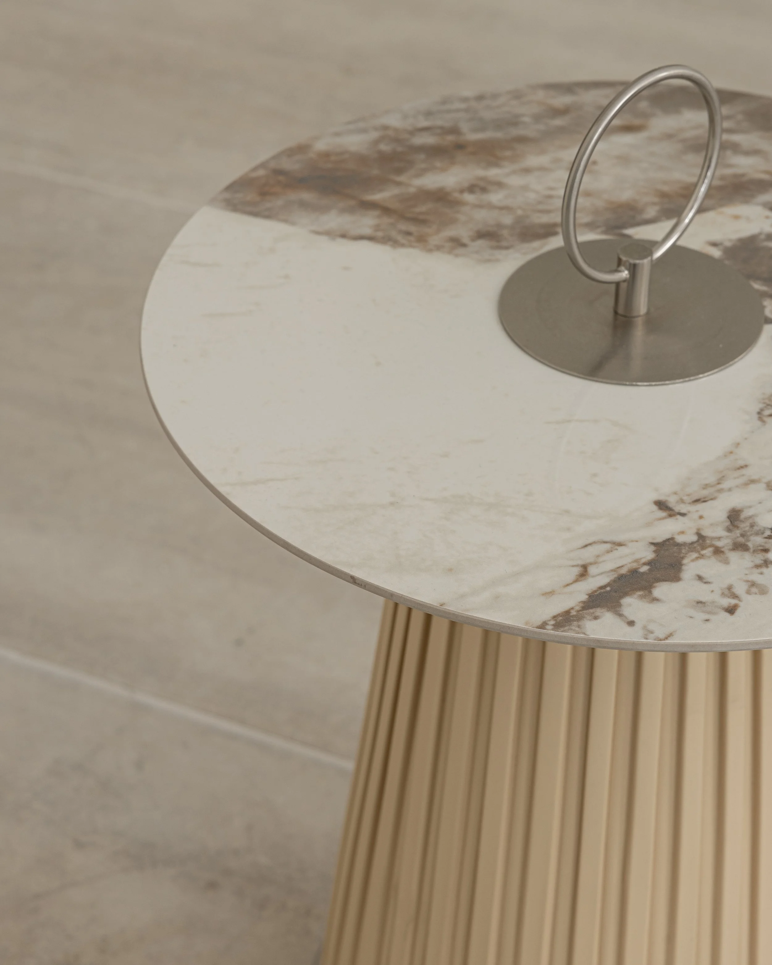 Close-up of a round marble-top side table with a metallic handle on the top, and wooden slats as its base, against a plain background.