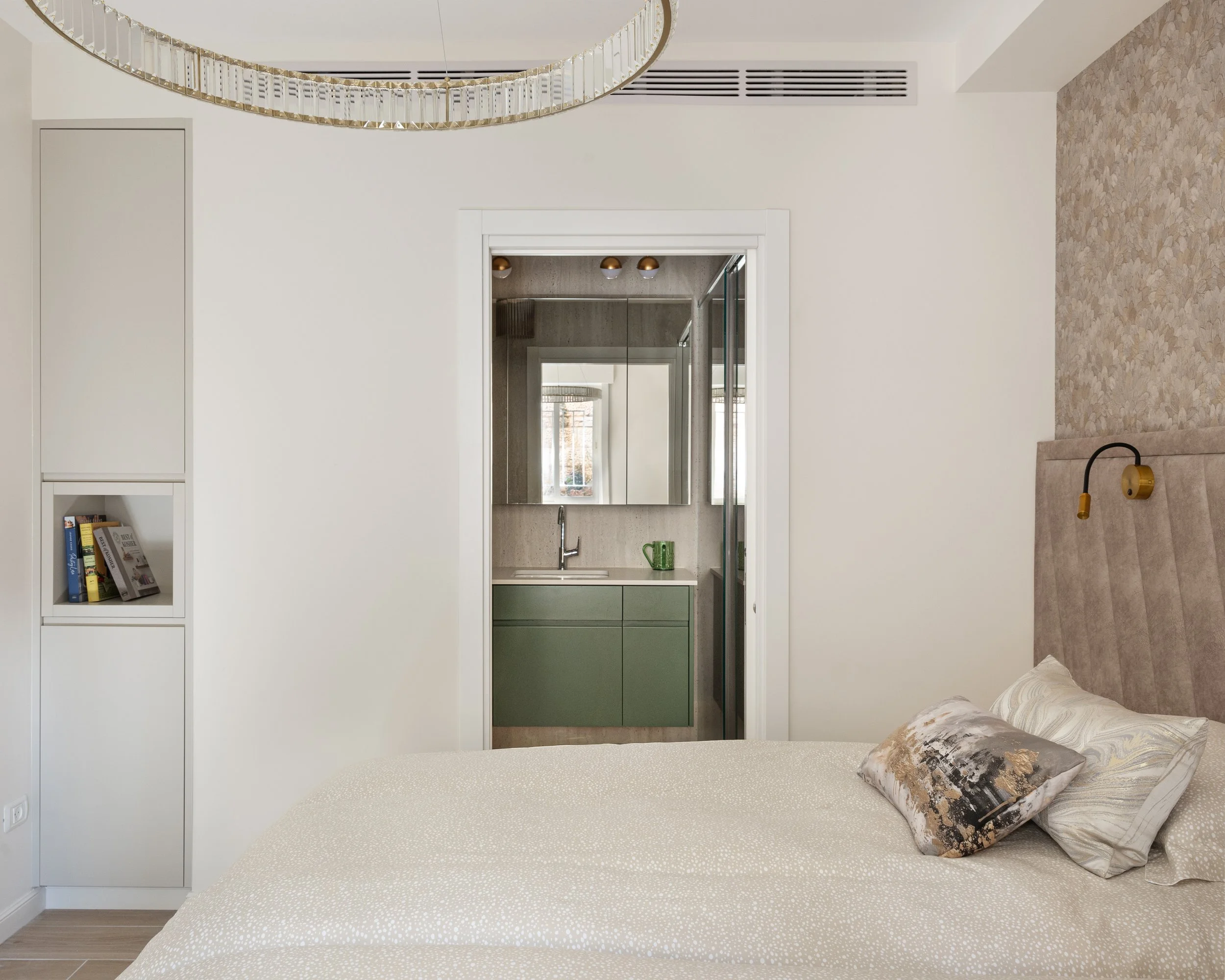 Modern bedroom with a bed, pillows, and a small open closet with books, a cabinet, and a mirror. There is a window in the distance, and a distinctive ceiling light fixture.