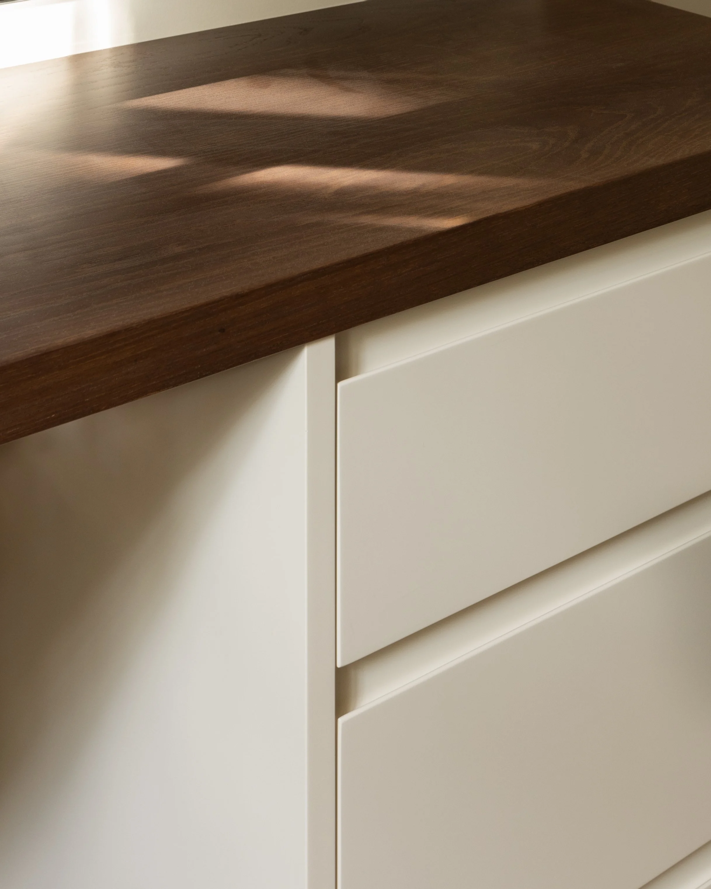 Close-up of a dark wooden table top with a smooth finish, and a white cabinet or drawer underneath, showing a corner with a gap.