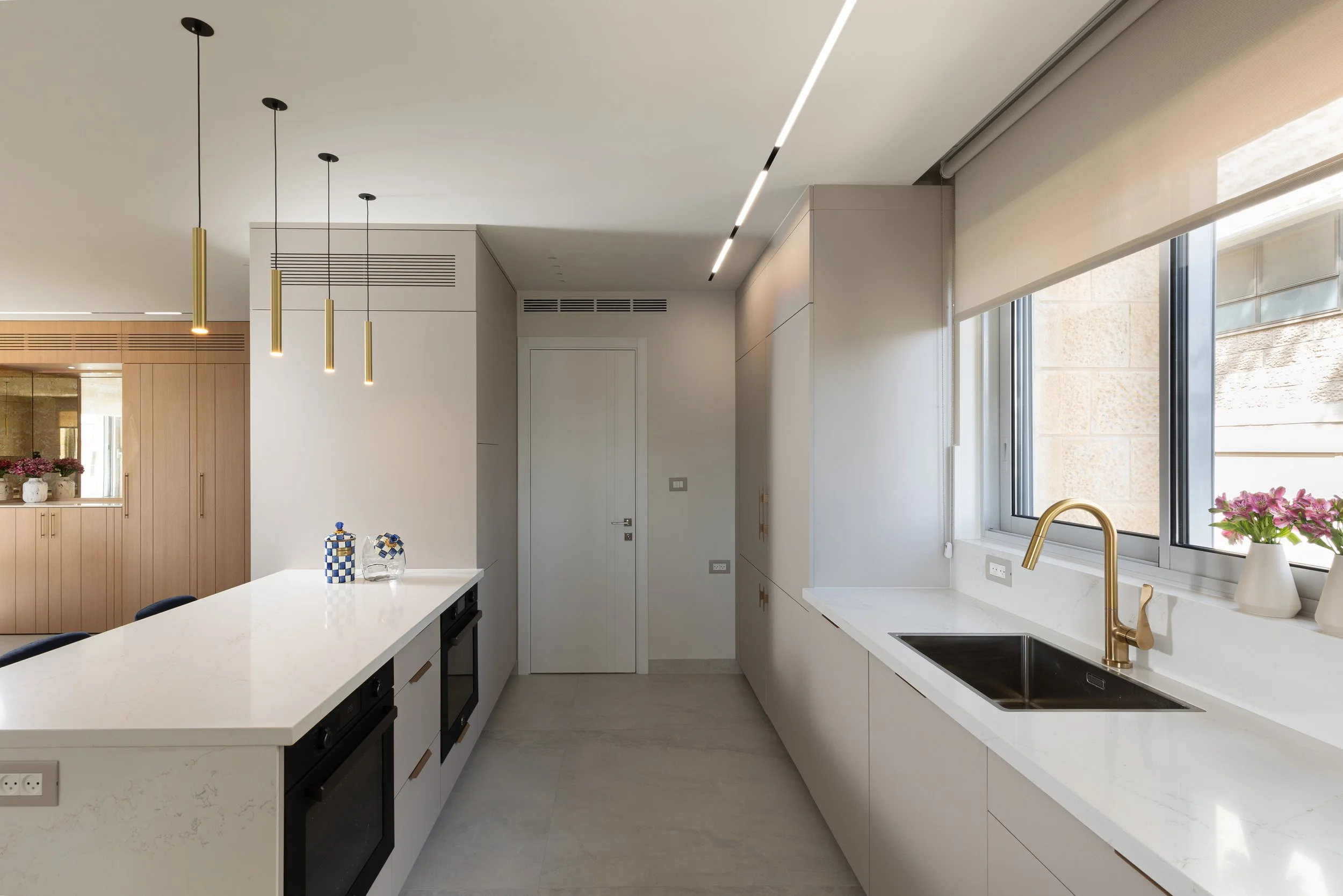 Modern kitchen with white countertops, gold faucet, large windows, and minimalist decor.
