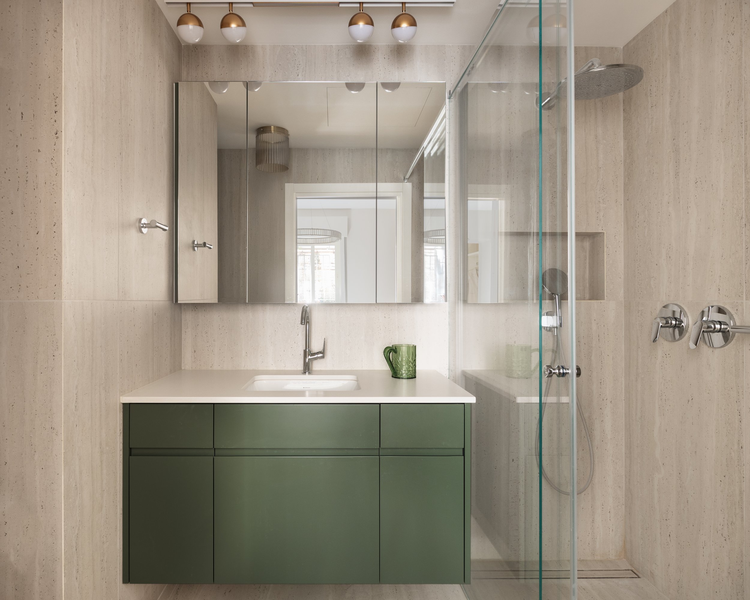 Modern bathroom with beige textured walls, a white sink, green cabinet, mirror, and glass walk-in shower with a rain shower head.