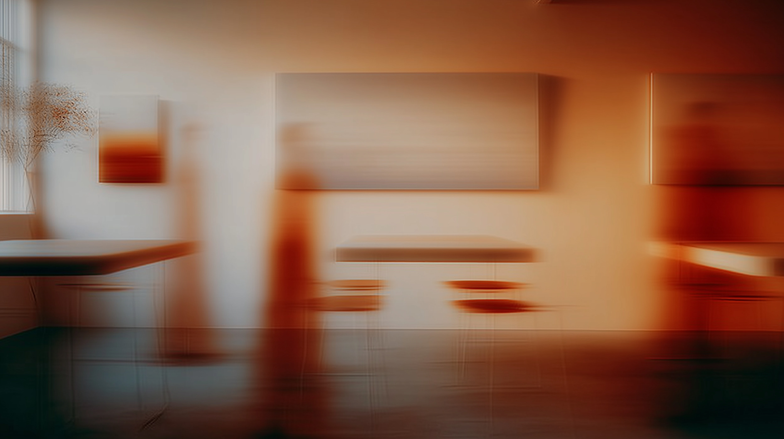 A blurred interior room with beige walls, abstract artwork on the walls, and a dark-colored table or countertop on the left side.