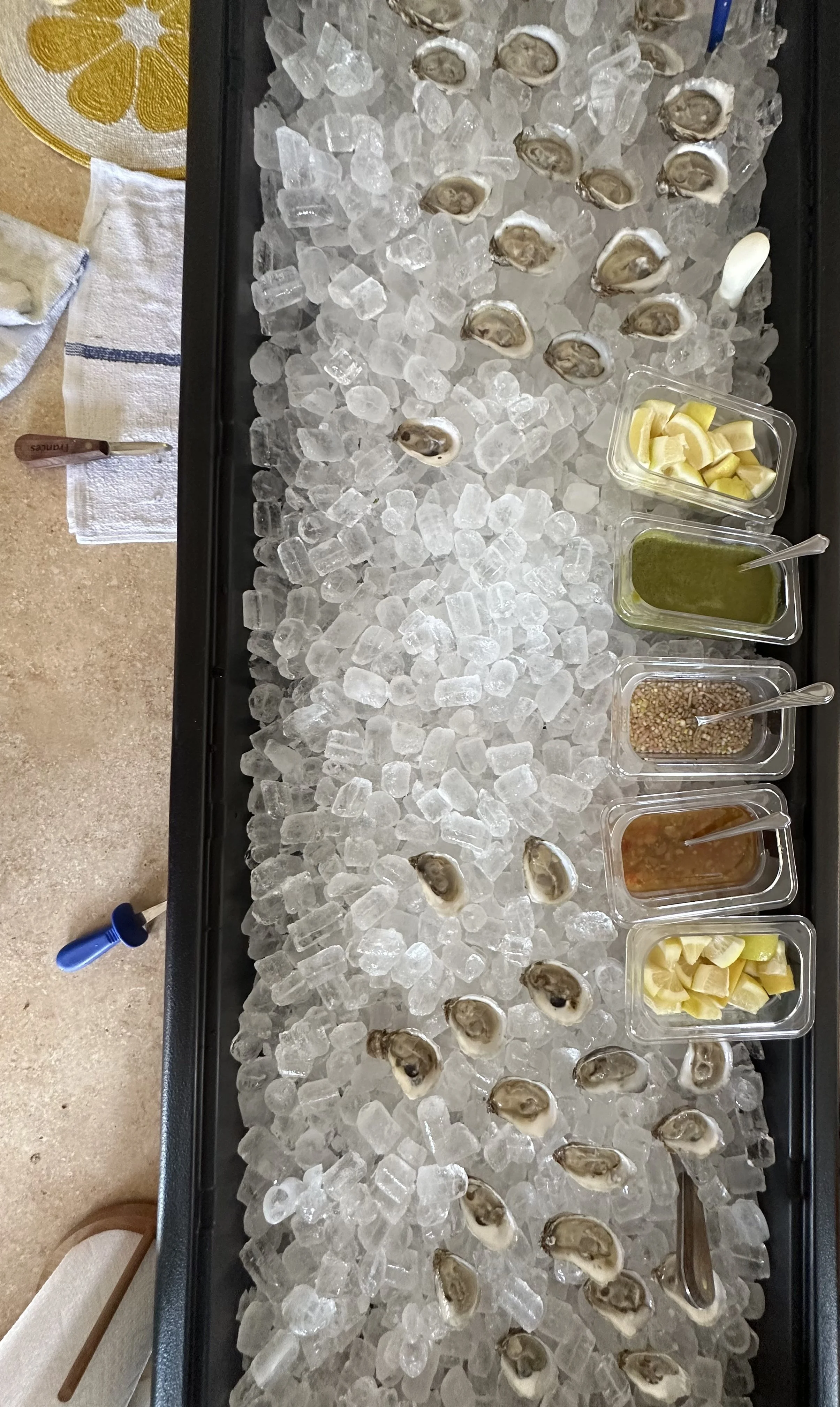 Fresh oysters on a bed of ice, served with lemon wedges, sauces, and condiments in small containers.