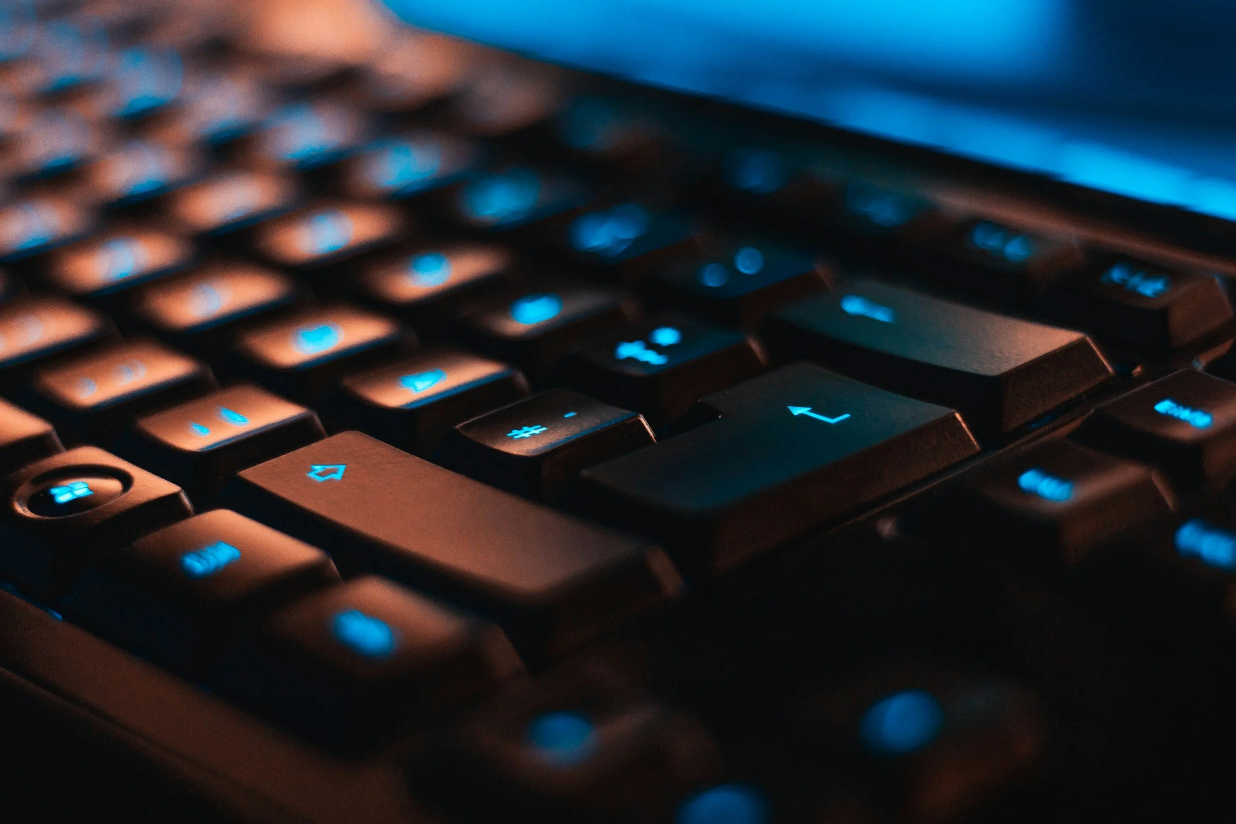Close-up of a computer keyboard with blue backlit keys, showing arrow and function keys.