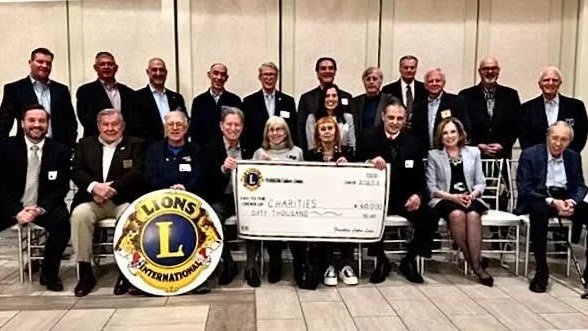 Group of people in formal attire posing indoors with a large check and a Lions Club International banner.
