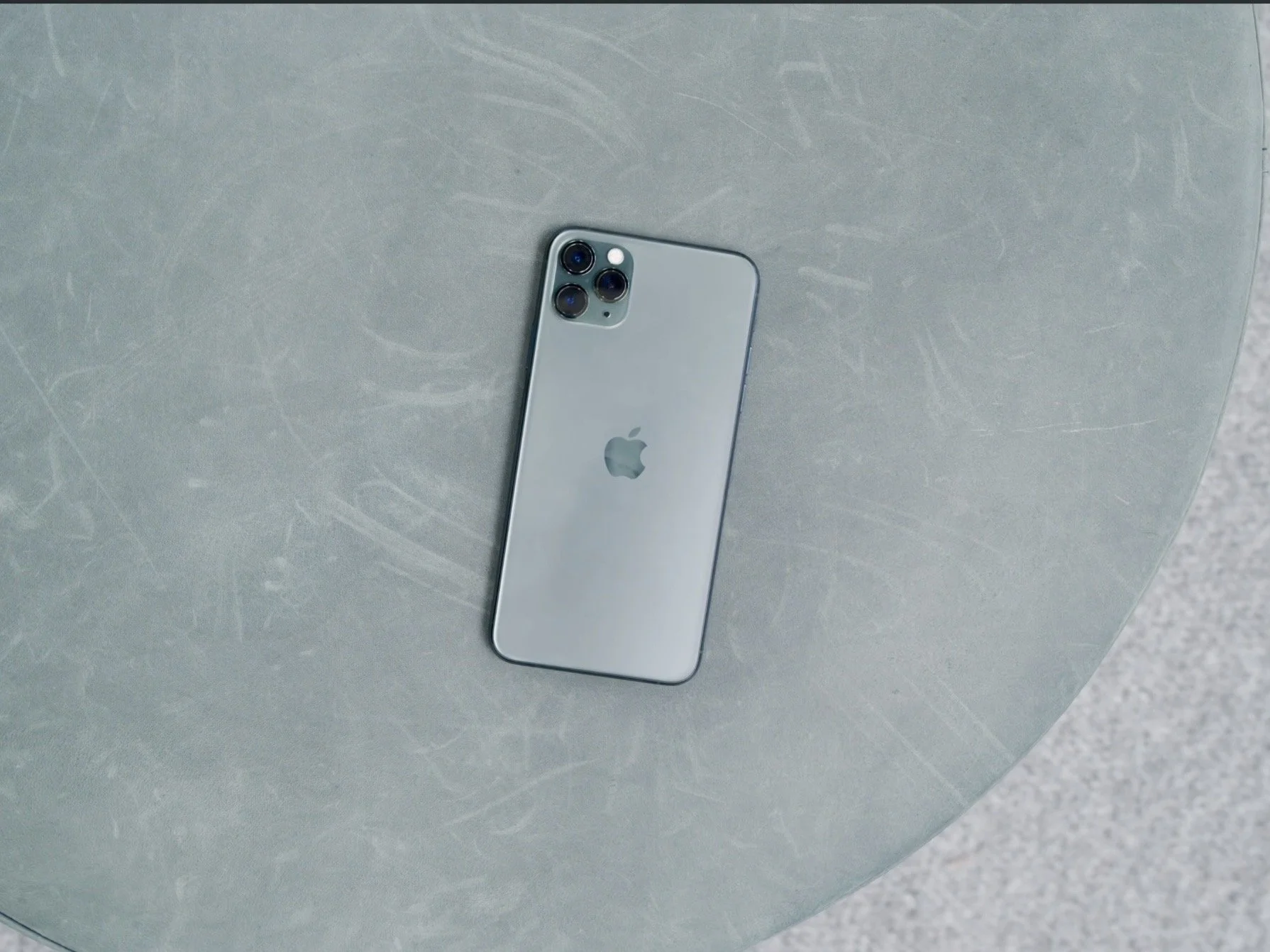 Silver Apple iPhone with triple camera setup and Apple logo on a gray textured surface