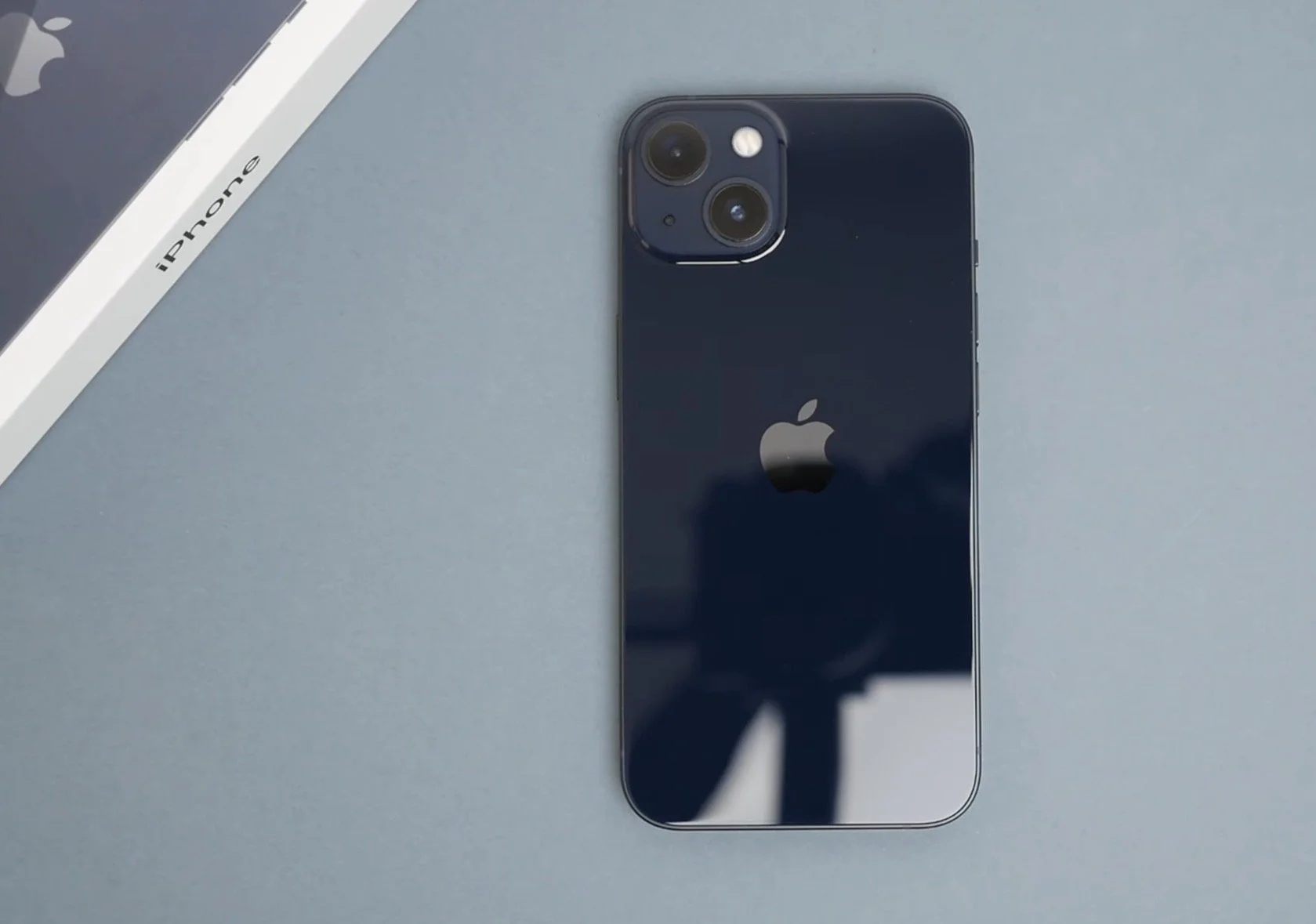 An iPhone with a black back, dual cameras, and the Apple logo, placed on a gray surface next to a box labeled 'iPhone'.