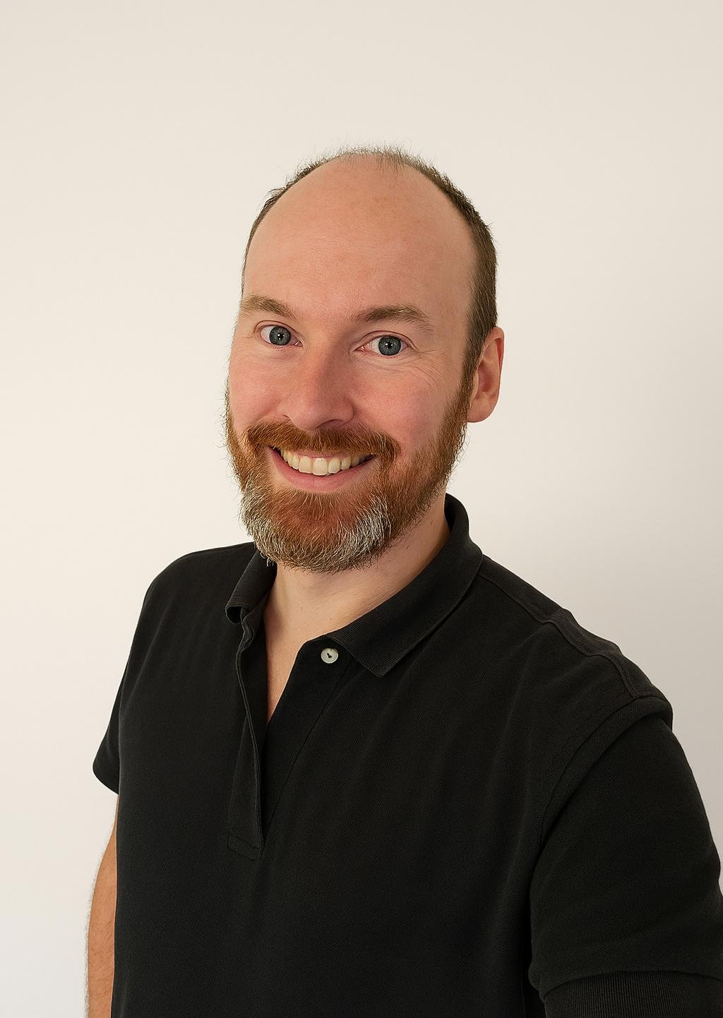 Ein Mann mit braunem Bart und kurzen Haaren trägt ein schwarzes Polo-Shirt und lächelt vor einem weißen Hintergrund.
Ein Bild zeigt den Baumanager und den Bauleiter und den Techniker