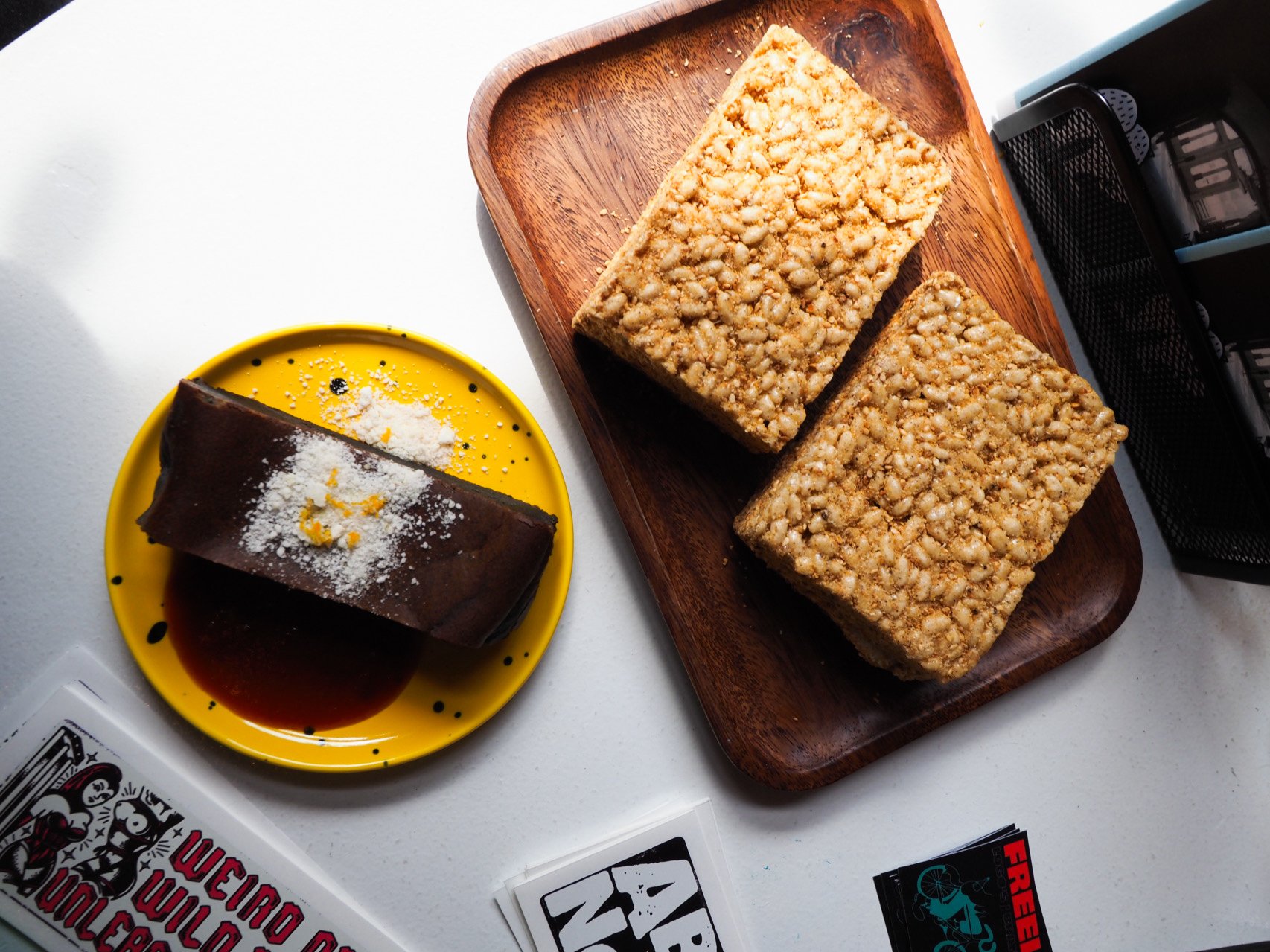 A chocolate treat on a yellow plate, and two rice crispy treats on a wooden platter
